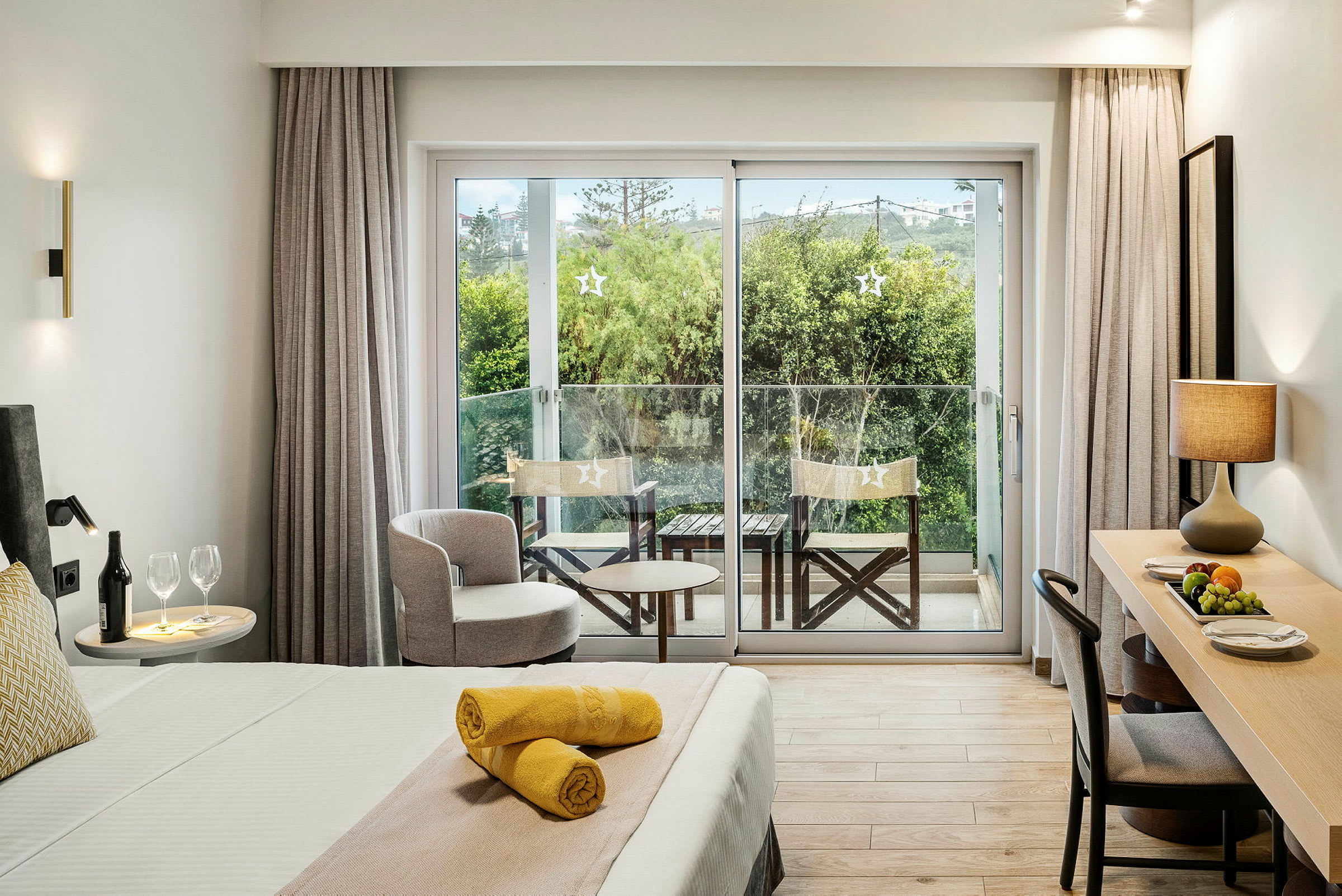 Et hotellrom med en oppredd seng, skrivebord og balkong med utsikt over grøntområder. (AI-generert tekst)