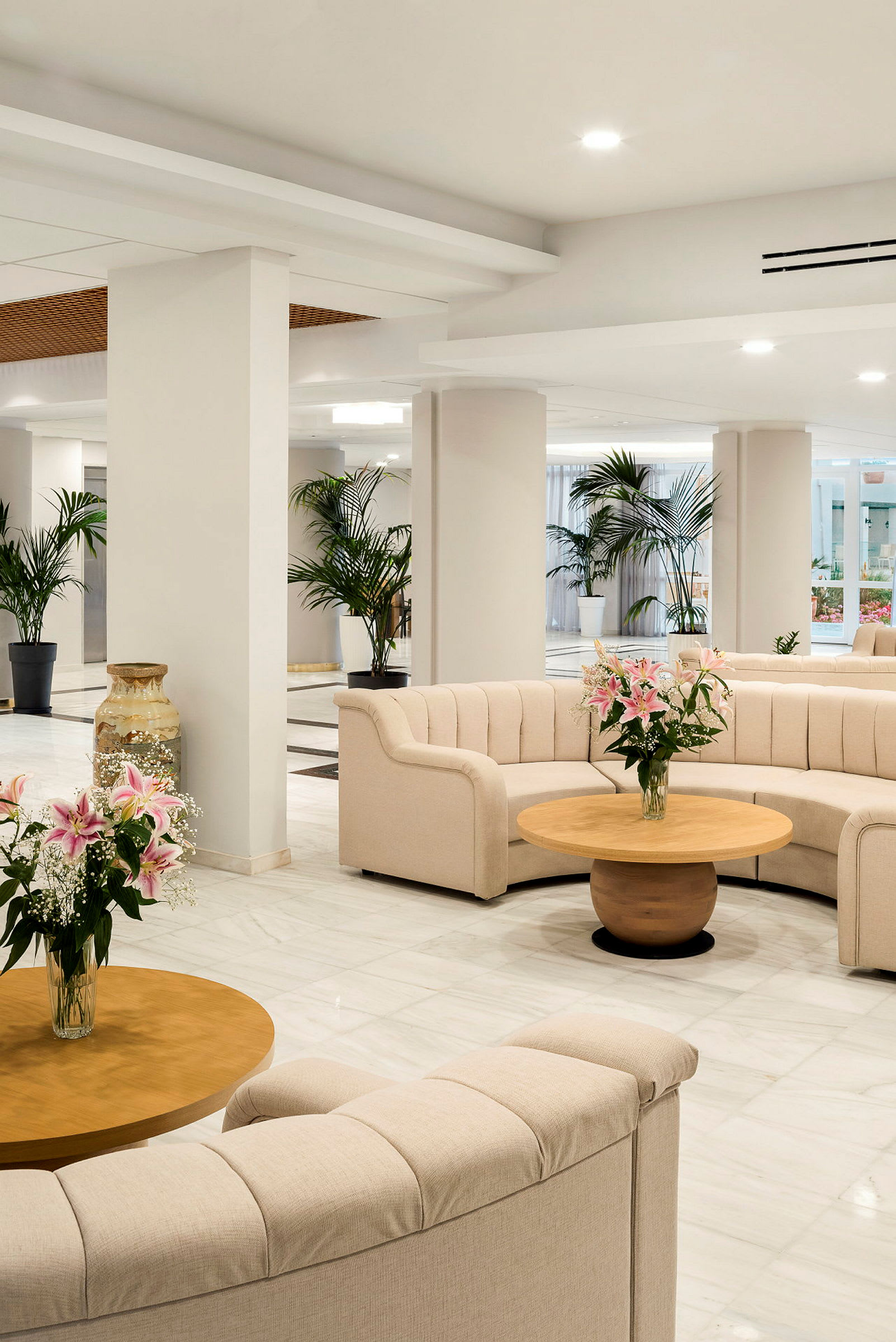 En lys og innbydende lounge med komfortable sofaer, runde bord og blomsterdekorasjoner. (AI-generert tekst)