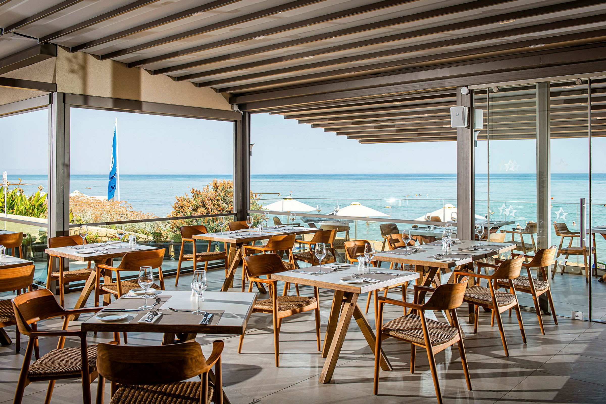Restaurant med moderne trebord og stoler, med utsikt over havet og stranden. (AI-generert tekst)