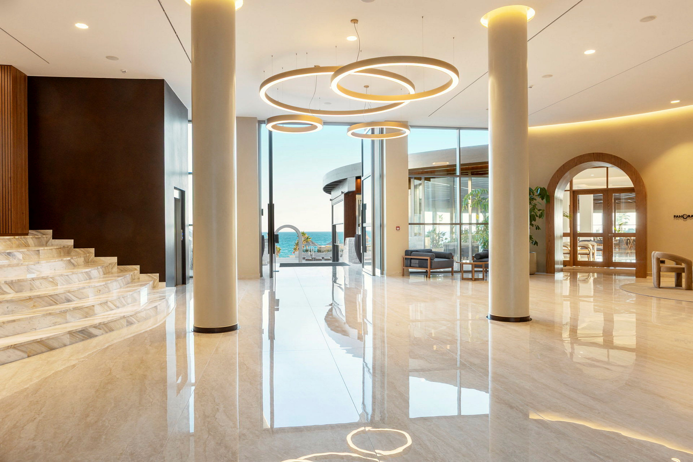 Lys og moderne lobby med store glasspartier og utsikt mot havet samt elegante taklamper. (AI-generert tekst)