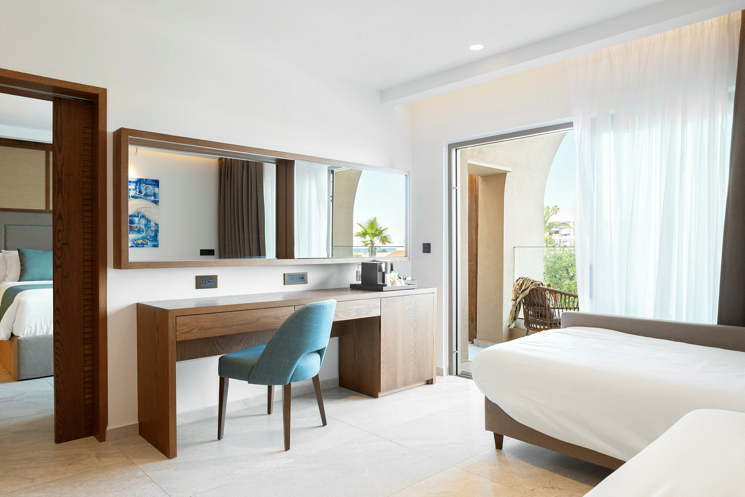 Et hotellrom med moderne interiør, inkludert en seng, et skrivebord med en stol og et speil. Rommet har en balkong med utsikt. (AI-generert tekst)