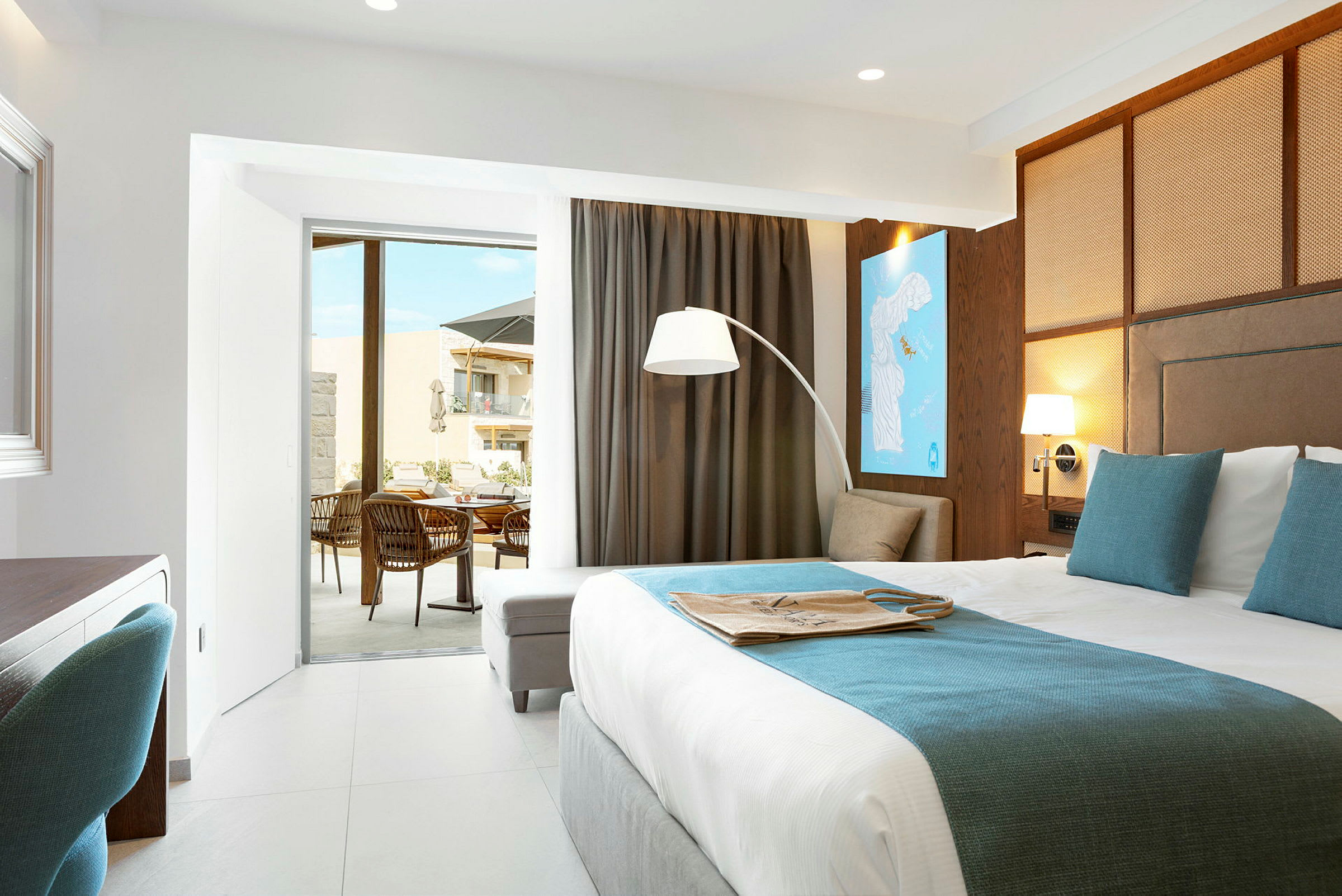 Et moderne hotellrom med en stor seng foran en glasskyvedør som leder til en møblert balkong. (AI-generert tekst)