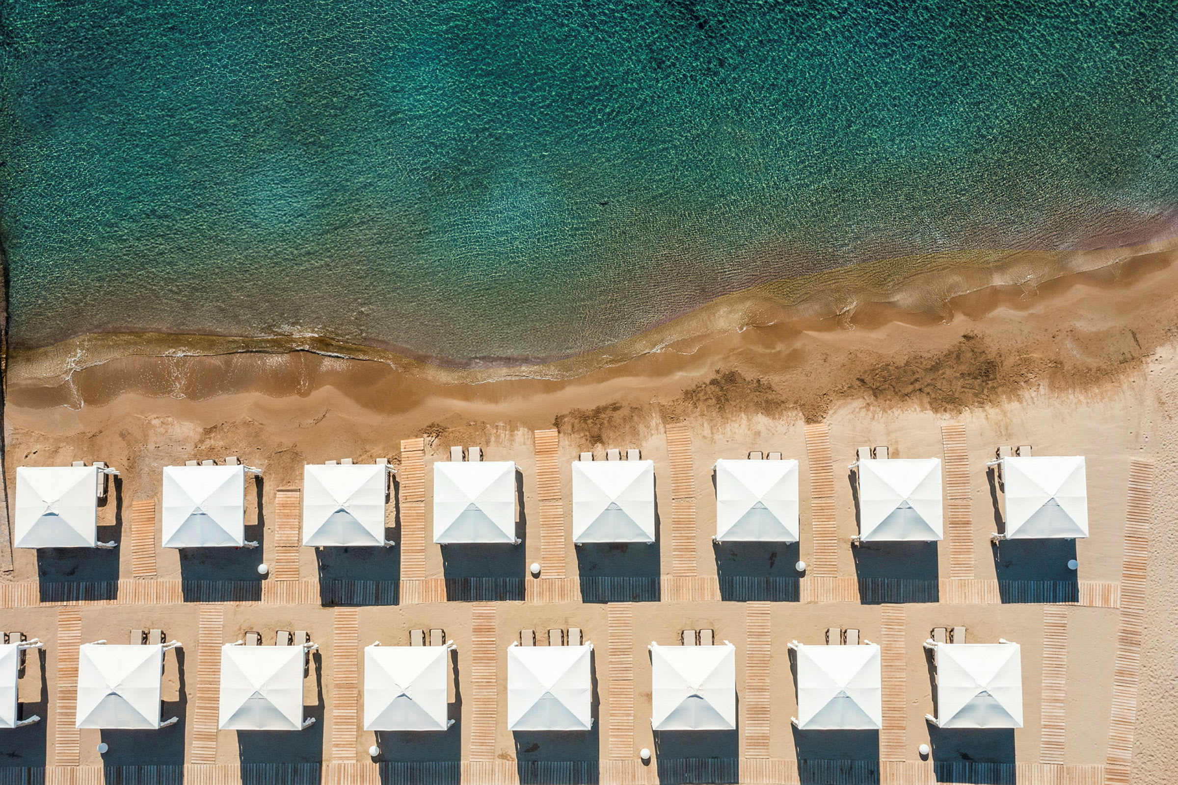 Bildet viser en rad med hvite strandpaviljonger på en sandstrand ved havet. (AI-generert tekst)