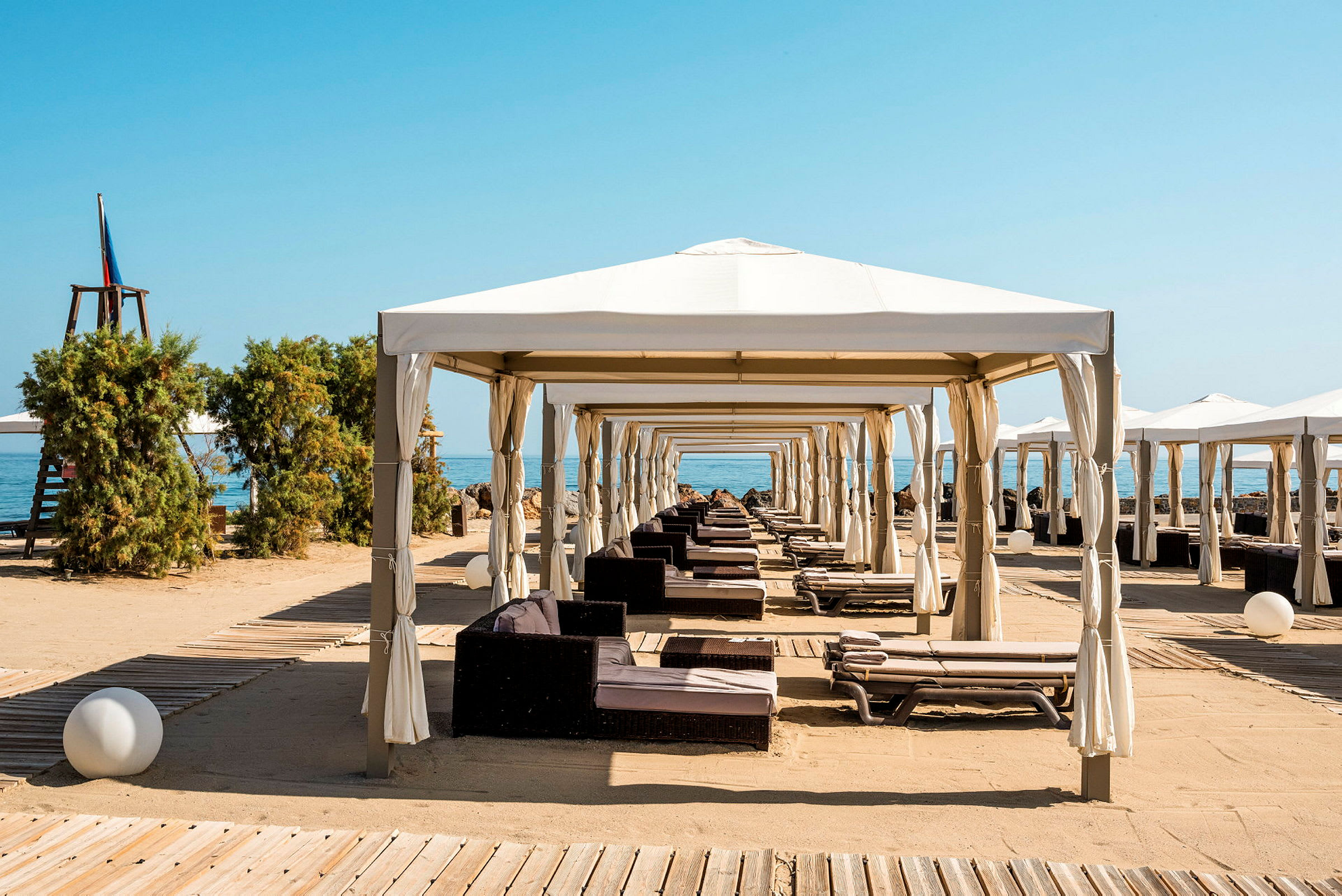 Strandpaviljonger med solsenger og sand. (AI-generert tekst)