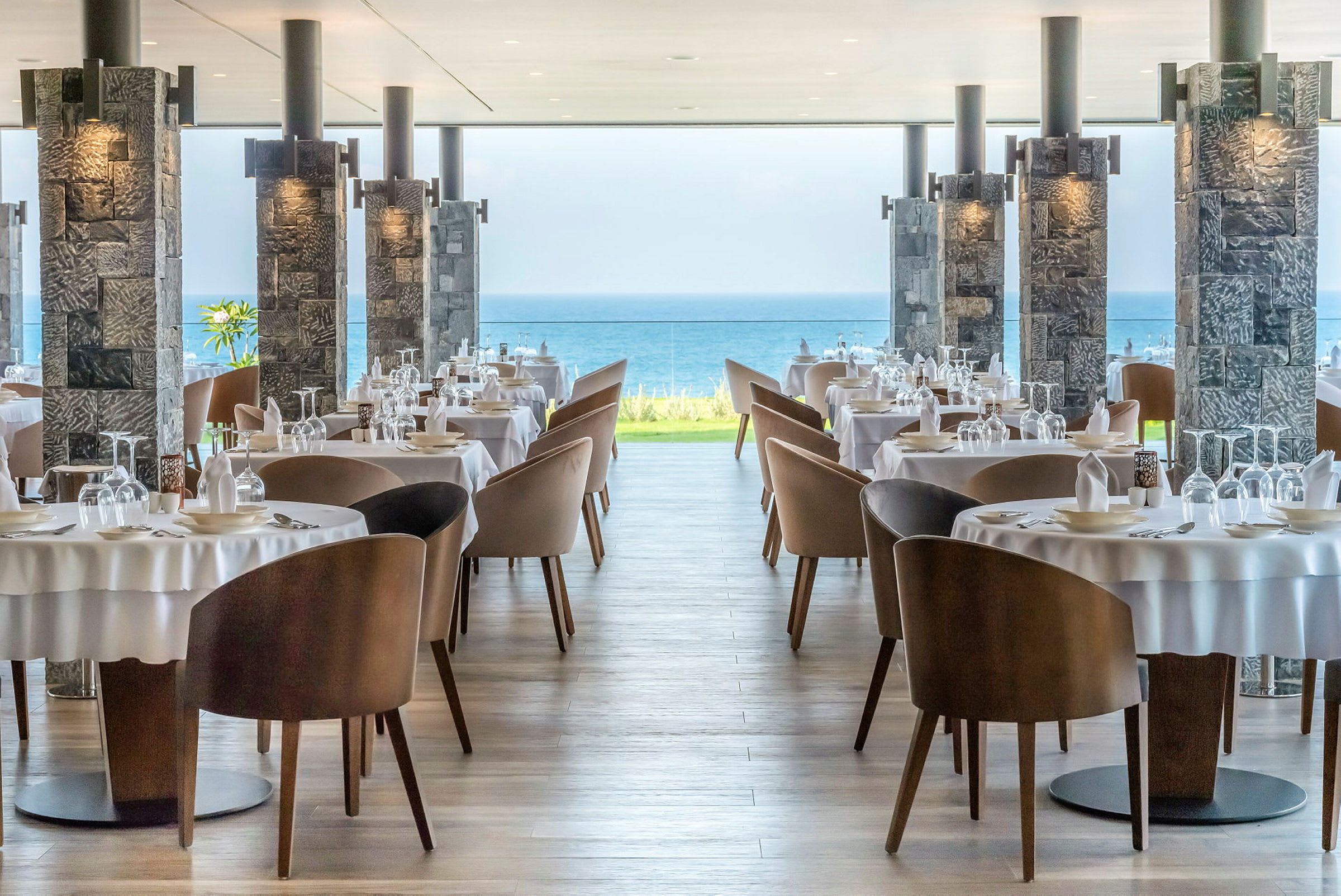 Restaurantbord med duker og stoler, havutsikt i bakgrunnen. (AI-generert tekst)