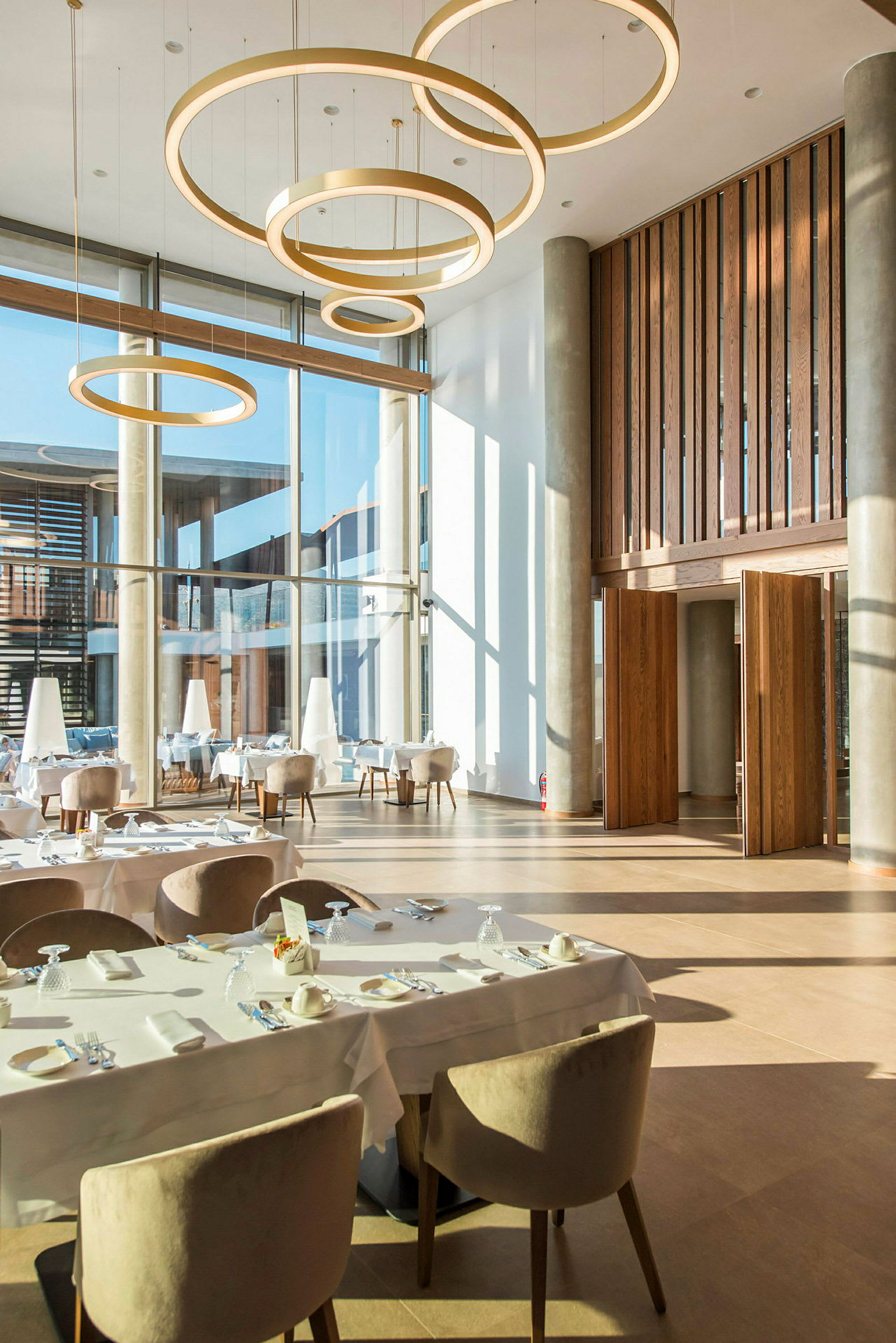 Interiør av en moderne restaurant med store vinduer og hengende sirkelrunde lamper. (AI-generert tekst)