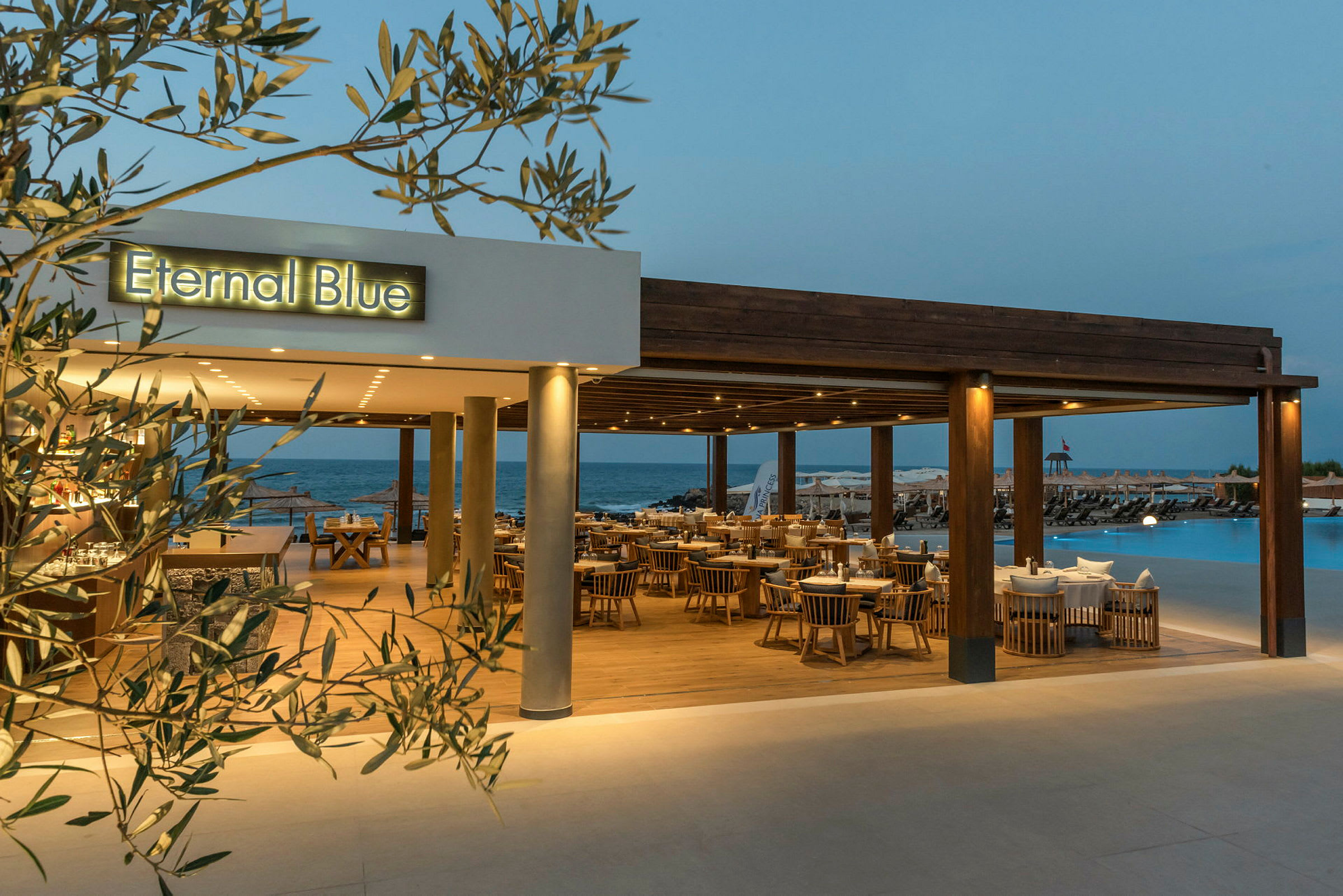 En restaurant med navnet 'Eternal Blue', med utsikt over et basseng og havet i bakgrunnen. (AI-generert tekst)