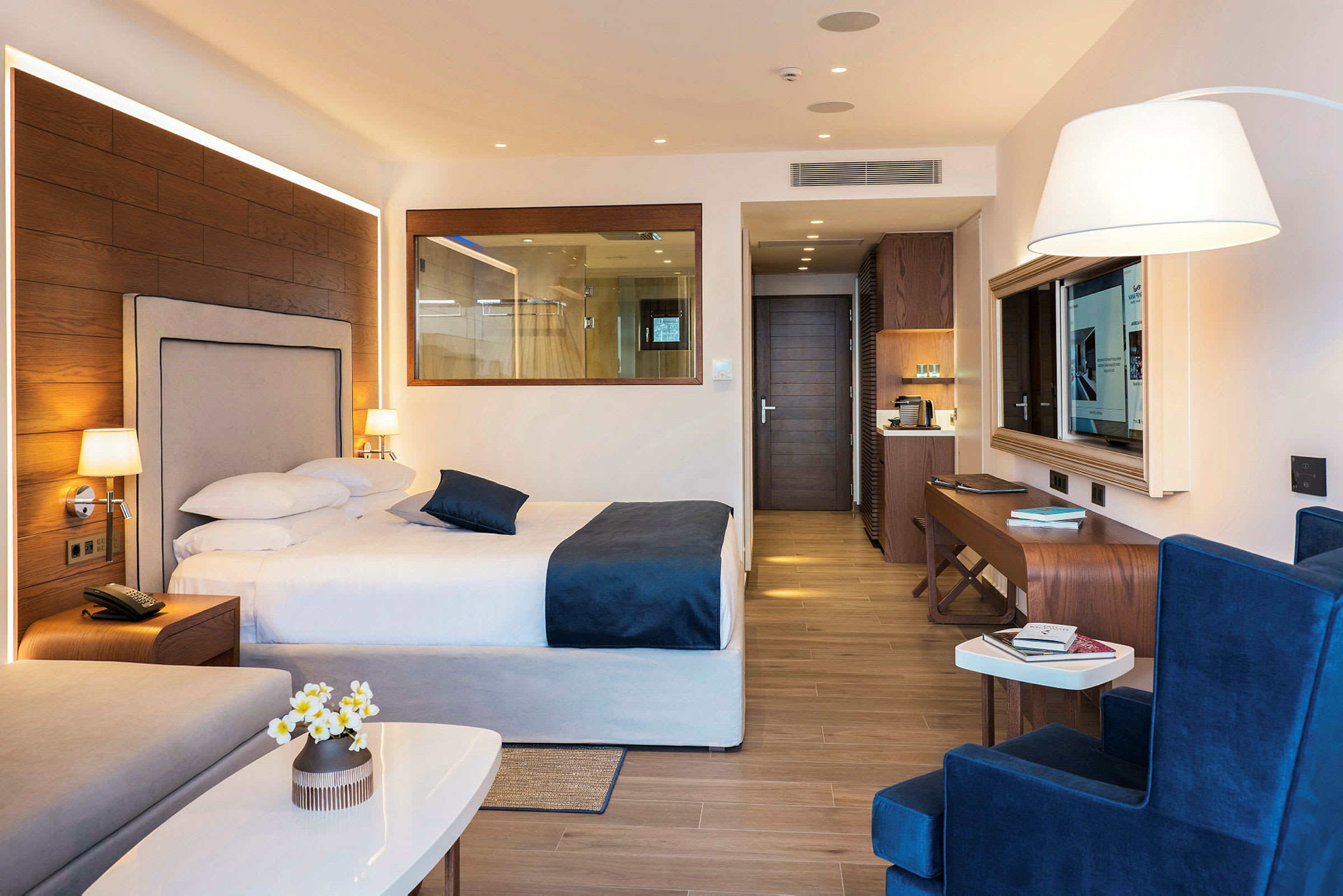 Hotellrom med dobbeltseng, sittegruppe og skrivebord, moderne innredet med tregulv. (AI-generert tekst)