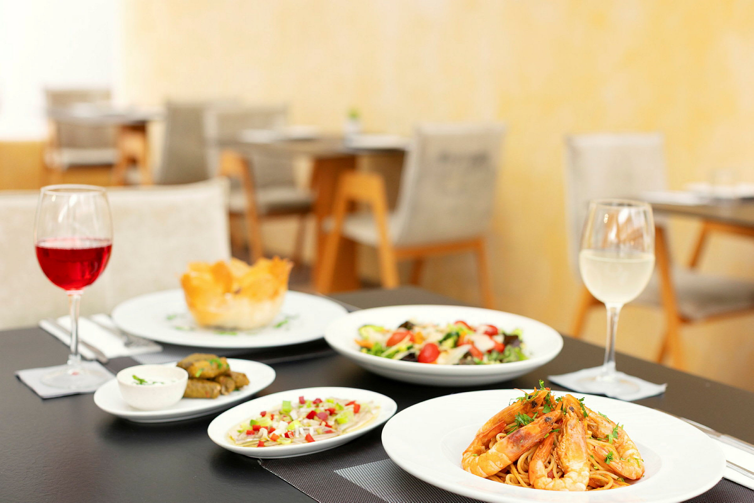 Bilde av et dekket bord med et måltid som inkluderer pasta med reker, salat, småretter og to glass vin. (AI-generert tekst)