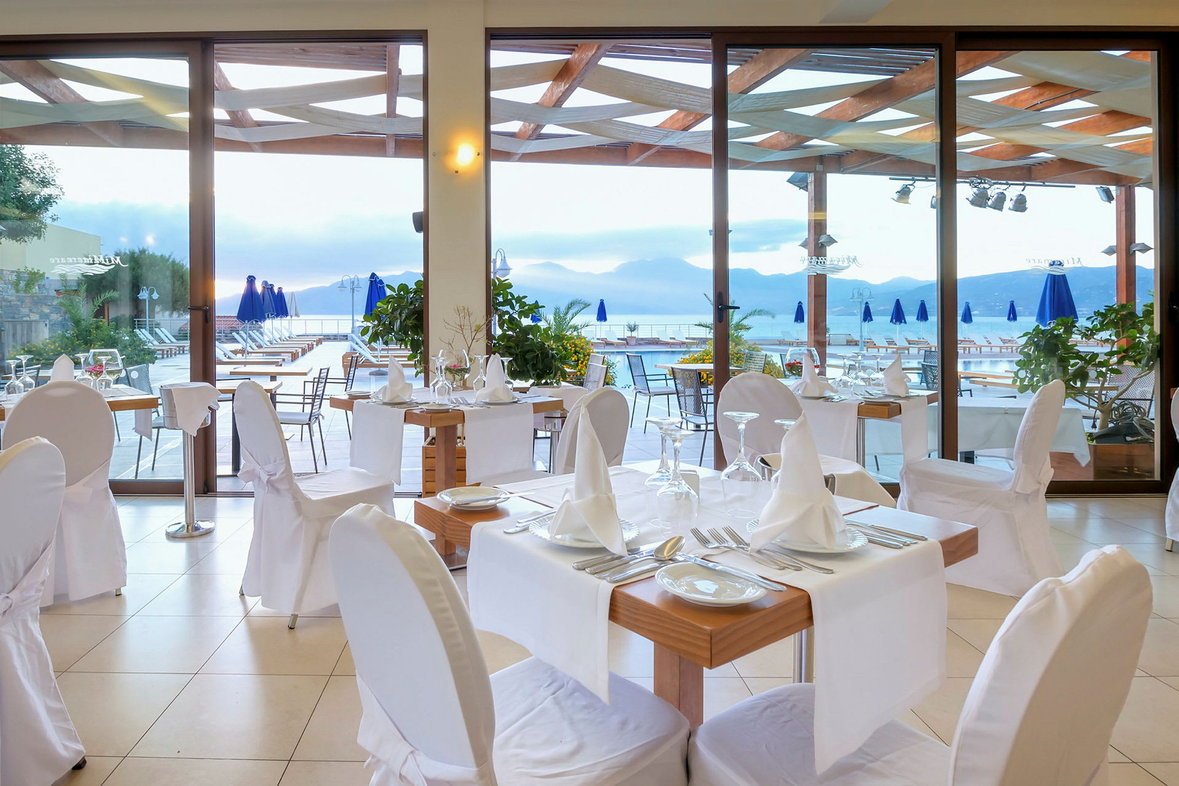 En restaurant med dekkede bord og stoler, på en terrasse med utsikt over fjell og vann. (AI-generert tekst)