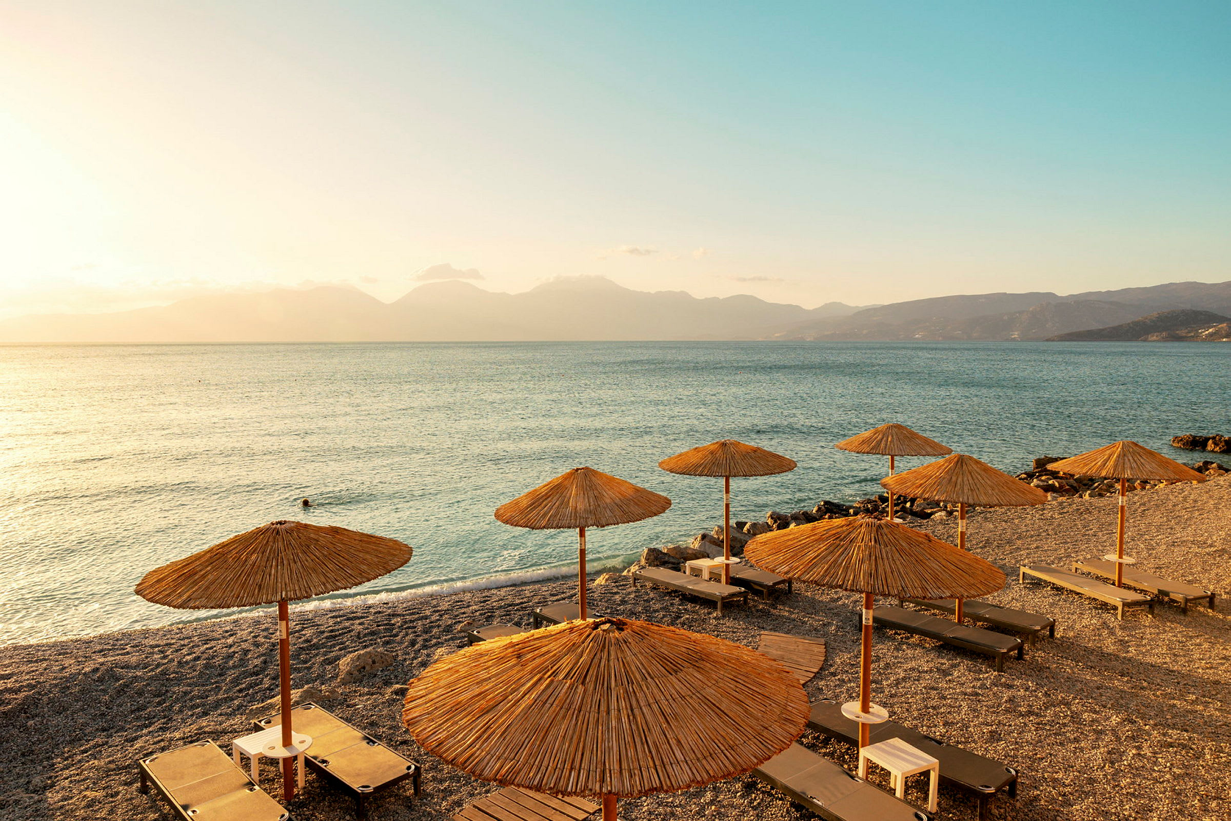 Strand med solsenger og parasoller, med utsikt over havet ved solnedgang. (AI-generert tekst)
