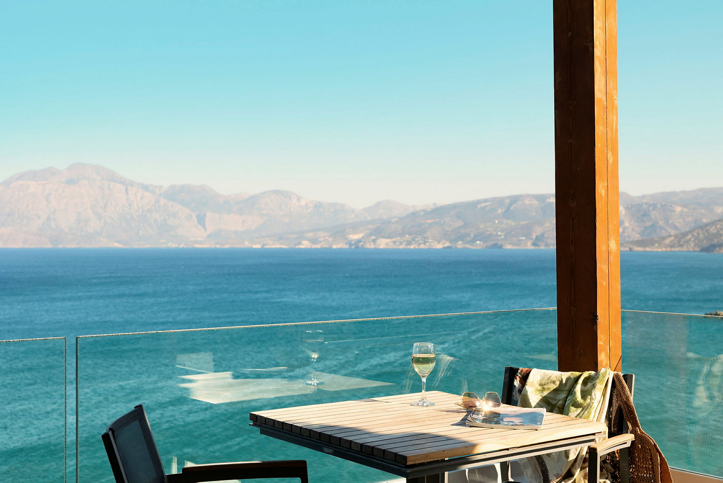 Bord og stoler på en terrasse med utsikt over havet og fjellene. (AI-generert tekst)