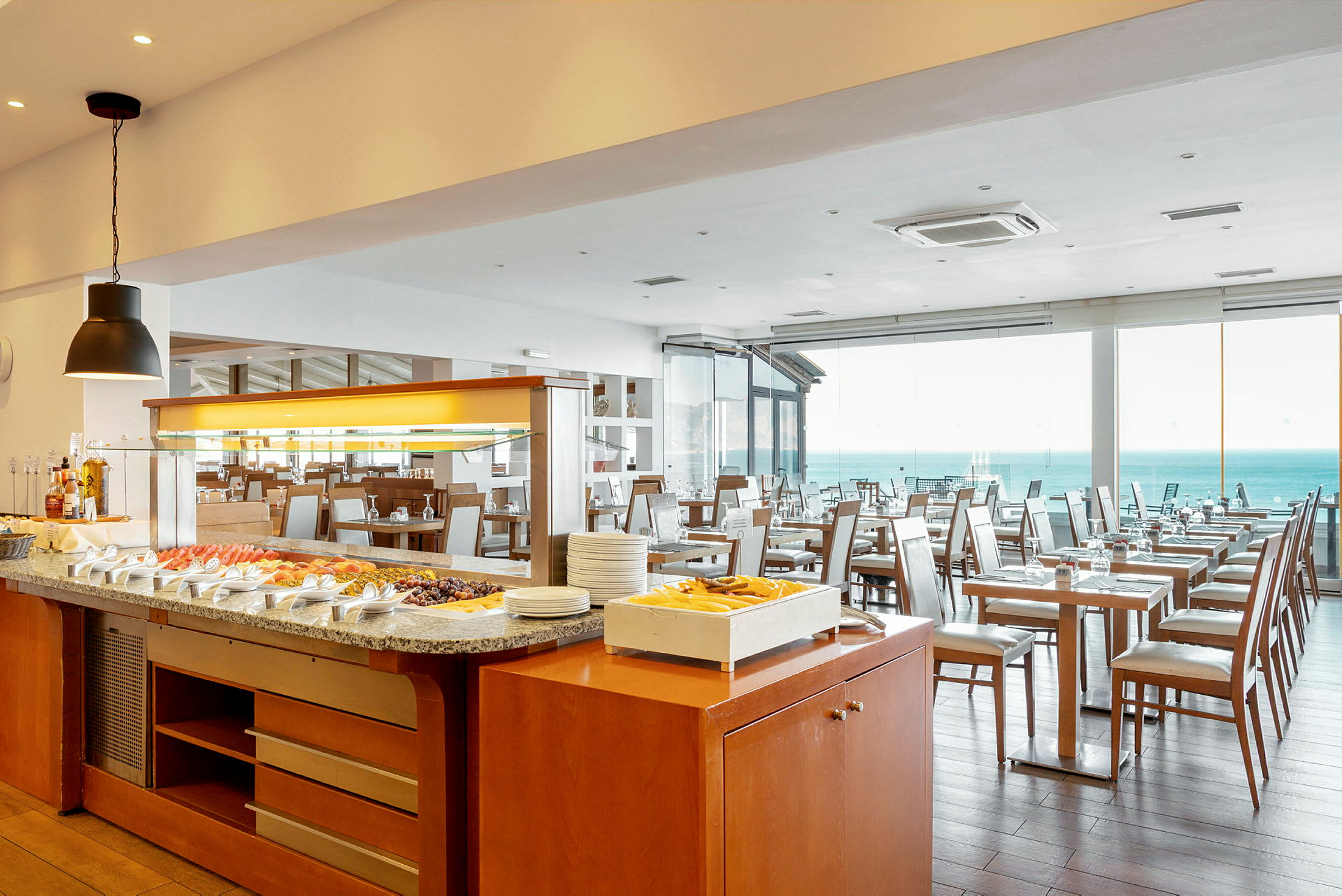 Bilde av en restaurant med buffébord og lyse stoler. Havet sees gjennom vinduene. (AI-generert tekst)