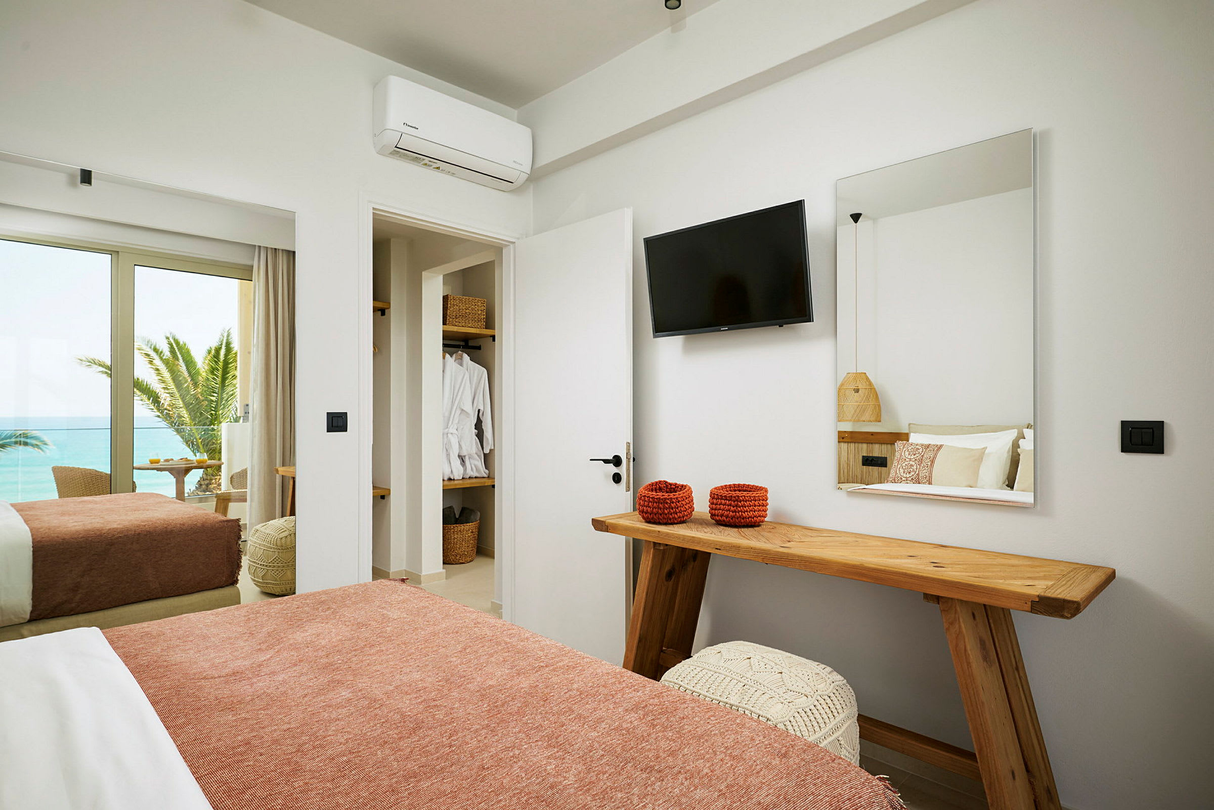 Hotellrom med seng, TV, speil og utsikt mot havet. (AI-generert tekst)