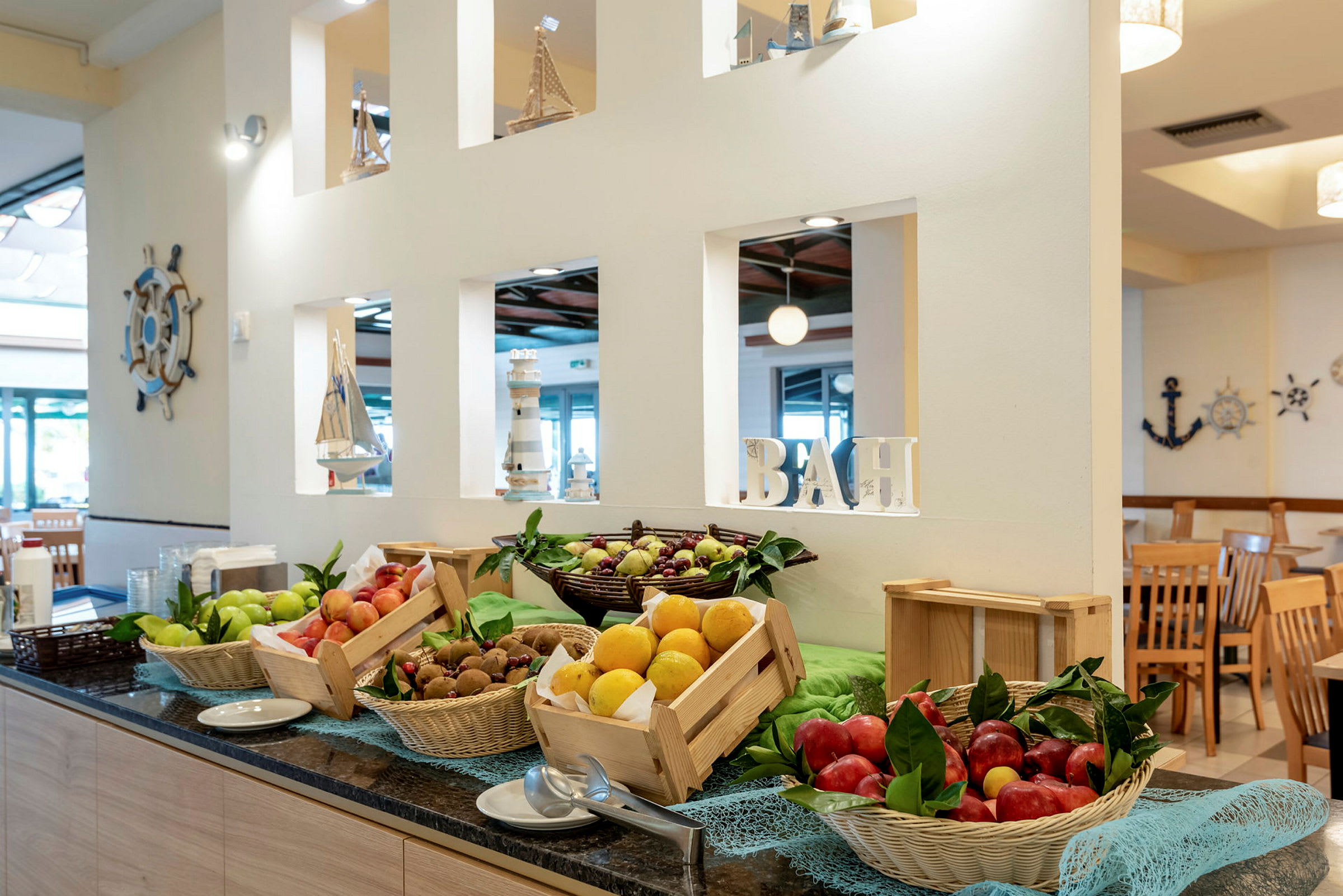 Et bord med kurver og kasser fylt med frukt, i en restaurant med nautisk interiør. (AI-generert tekst)