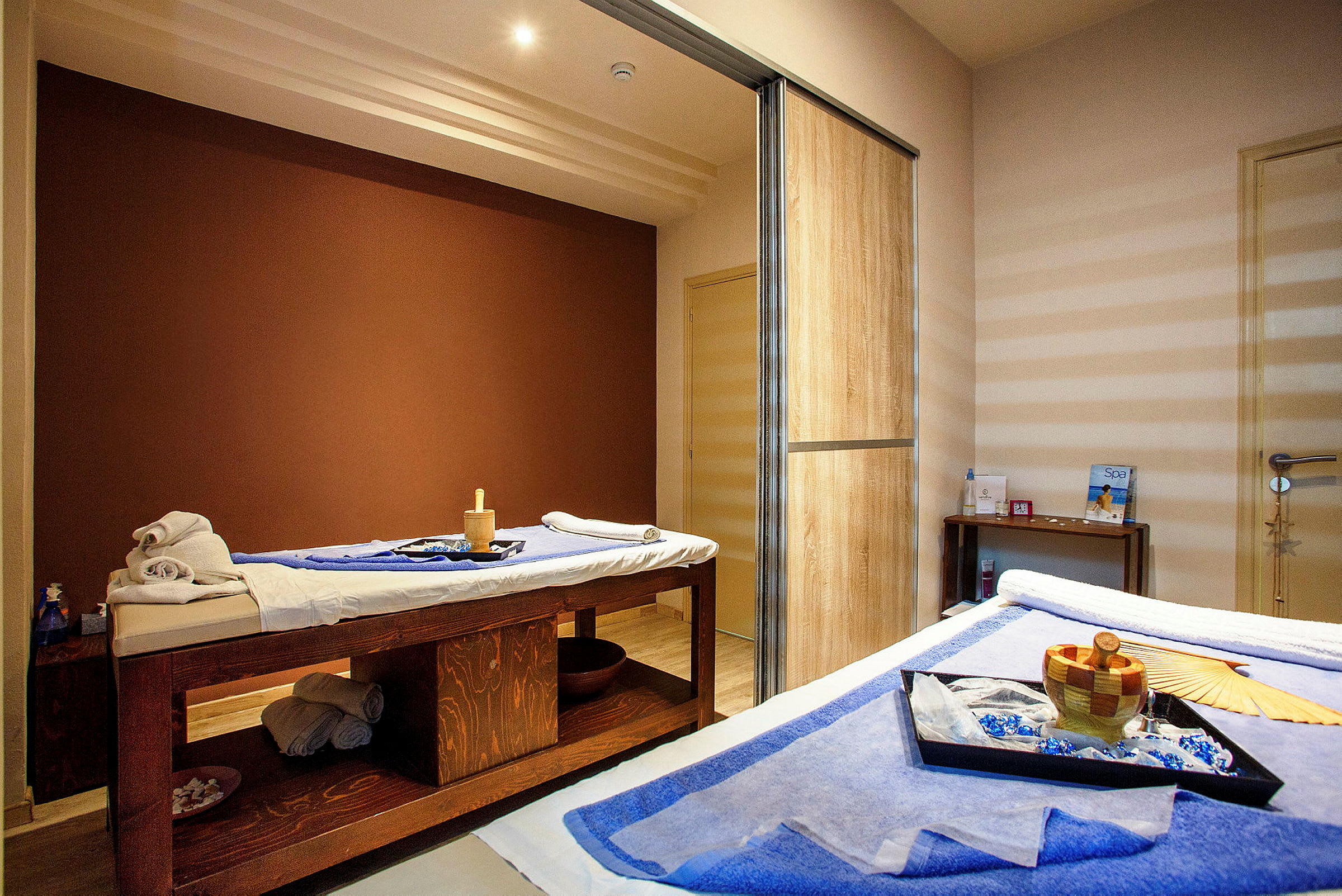 Et rom med terapeutiske behandlingsbord dekket med håndklær og spa-tilbehør. (AI-generert tekst)
