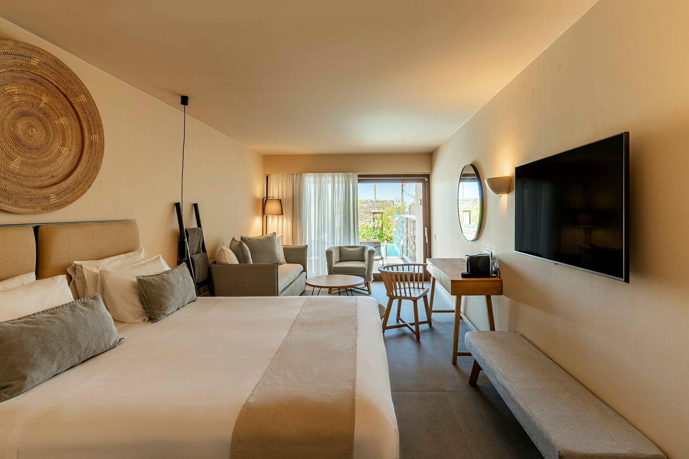 Et moderne hotellrom med en stor seng, en sofa, en TV på veggen og et skrivebord med stol. Rommet har en uteplass med bassengutsikt. (AI-generert tekst)