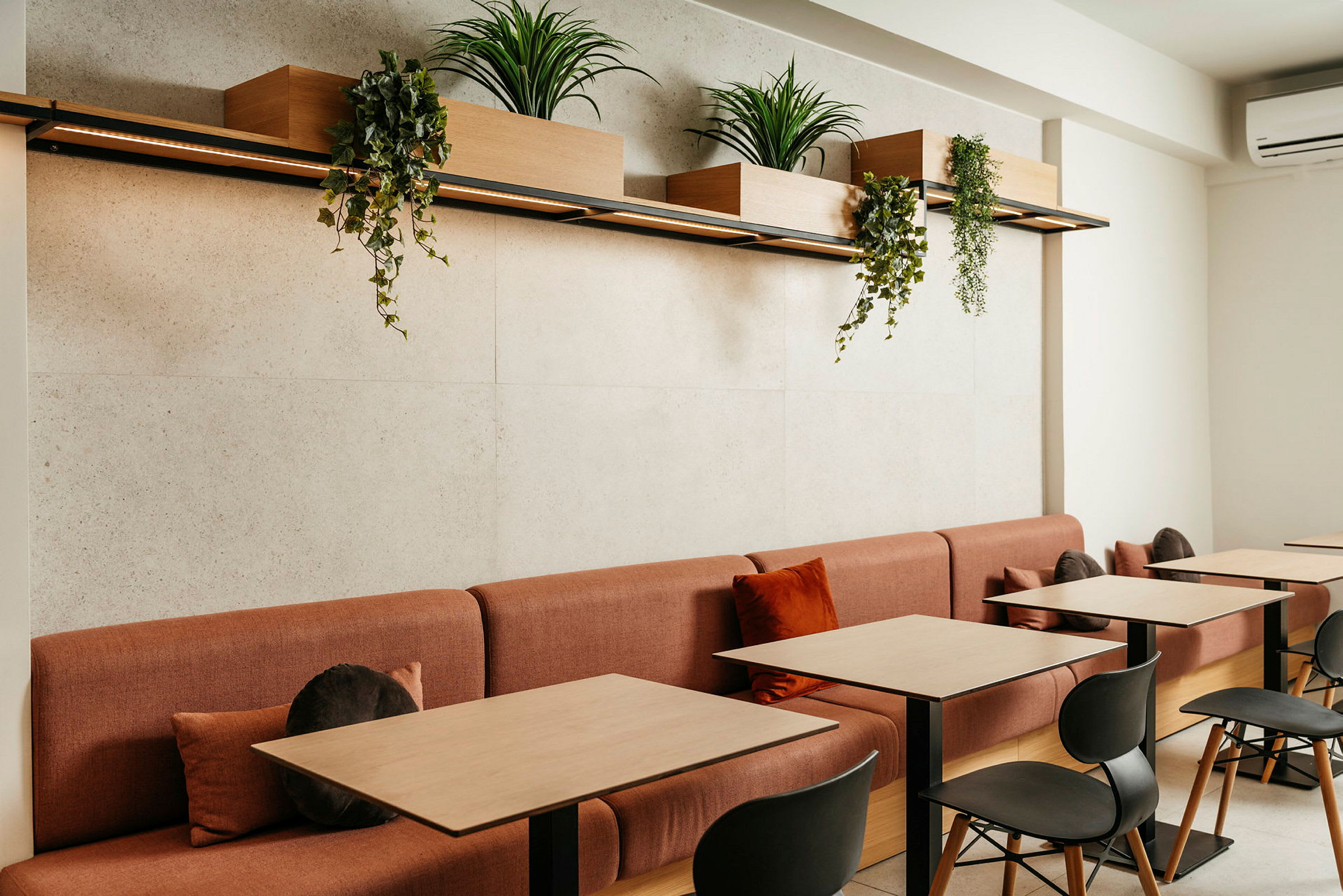 Et moderne kaféområde med røde sofaer og bord i tre, dekorert med plantekasser som henger over. (AI-generert tekst)