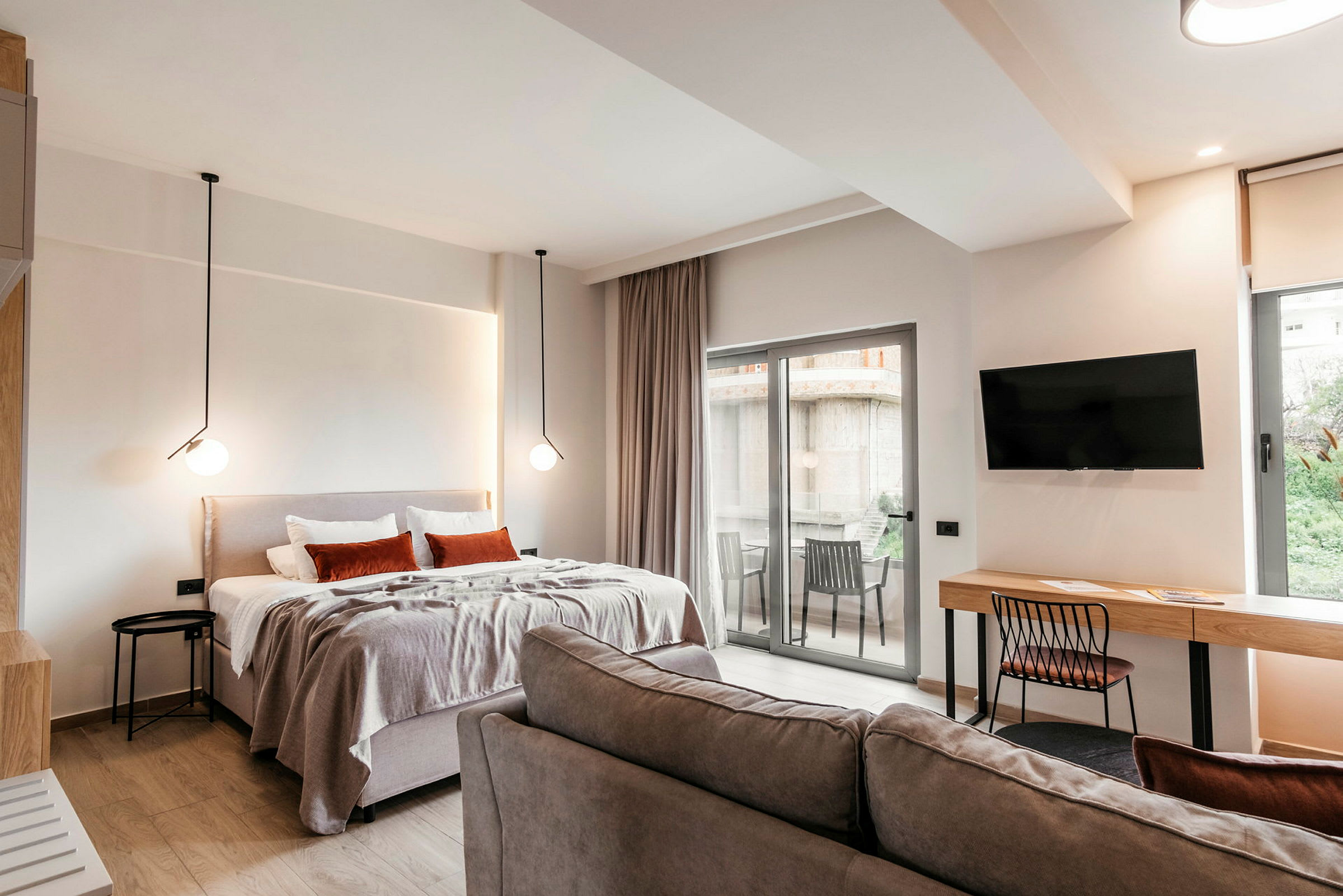 Et moderne hotellrom med seng, sofa, skrivebord, TV og en balkong med utsikt. (AI-generert tekst)