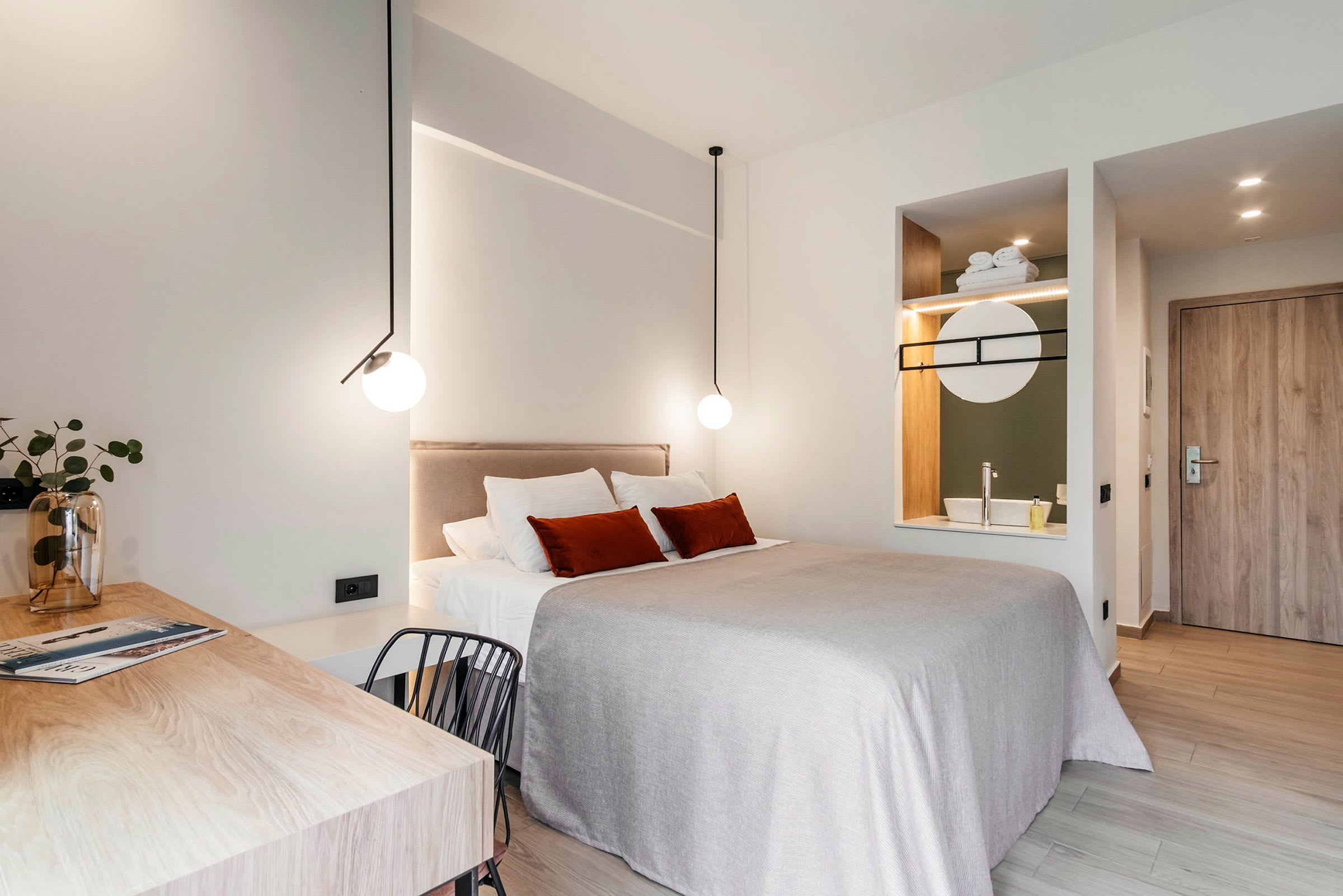 Et moderne innredet hotellrom med en dobbeltseng, skrivebord og integrert vask med speil. (AI-generert tekst)