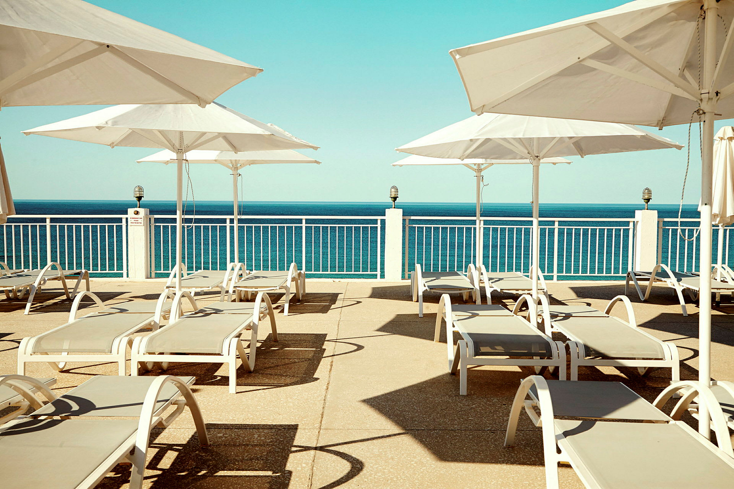 Utsikt over en solterrasse med solsenger og parasoller, med havet i bakgrunnen. (AI-generert tekst)