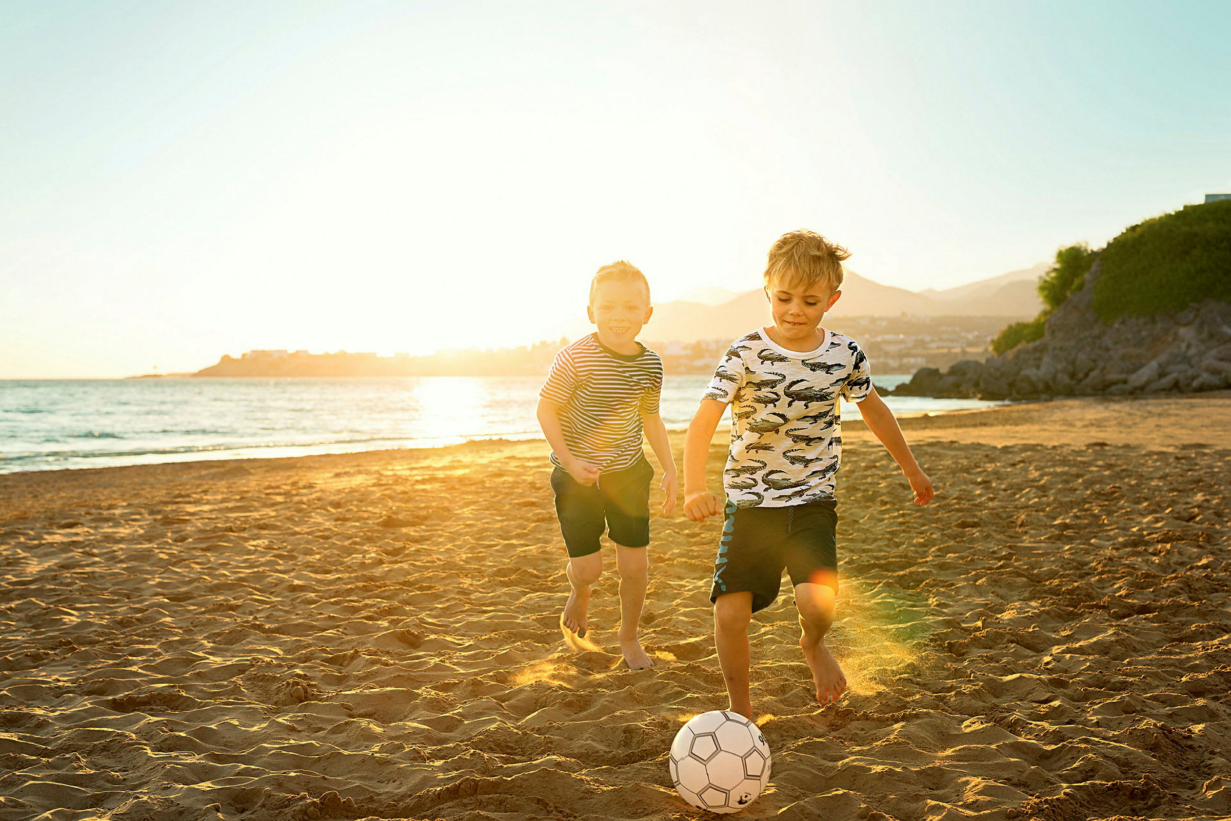 To barn spiller fotball på en solrik strand. (AI-generert tekst)