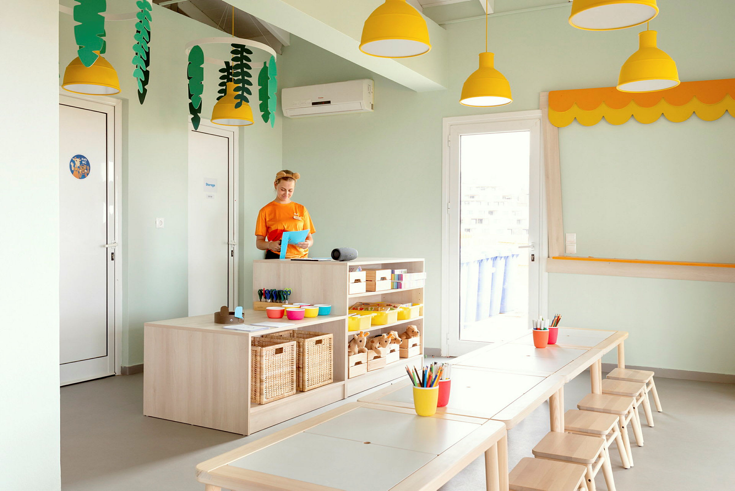 Et fargerikt rom med bord, stoler og oppbevaringshyller fylt med pedagogisk materiell. (AI-generert tekst)