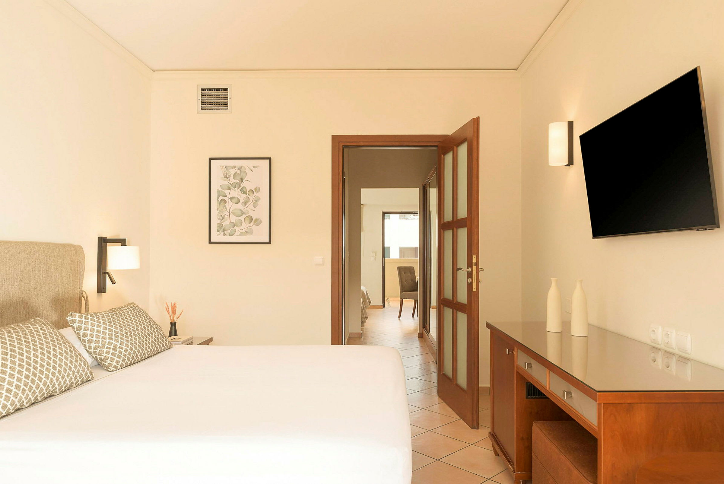 Hotellrom med en dobbeltseng, sengelamper, en veggmontert TV og et skrivebord med dekorative gjenstander. (AI-generert tekst)
