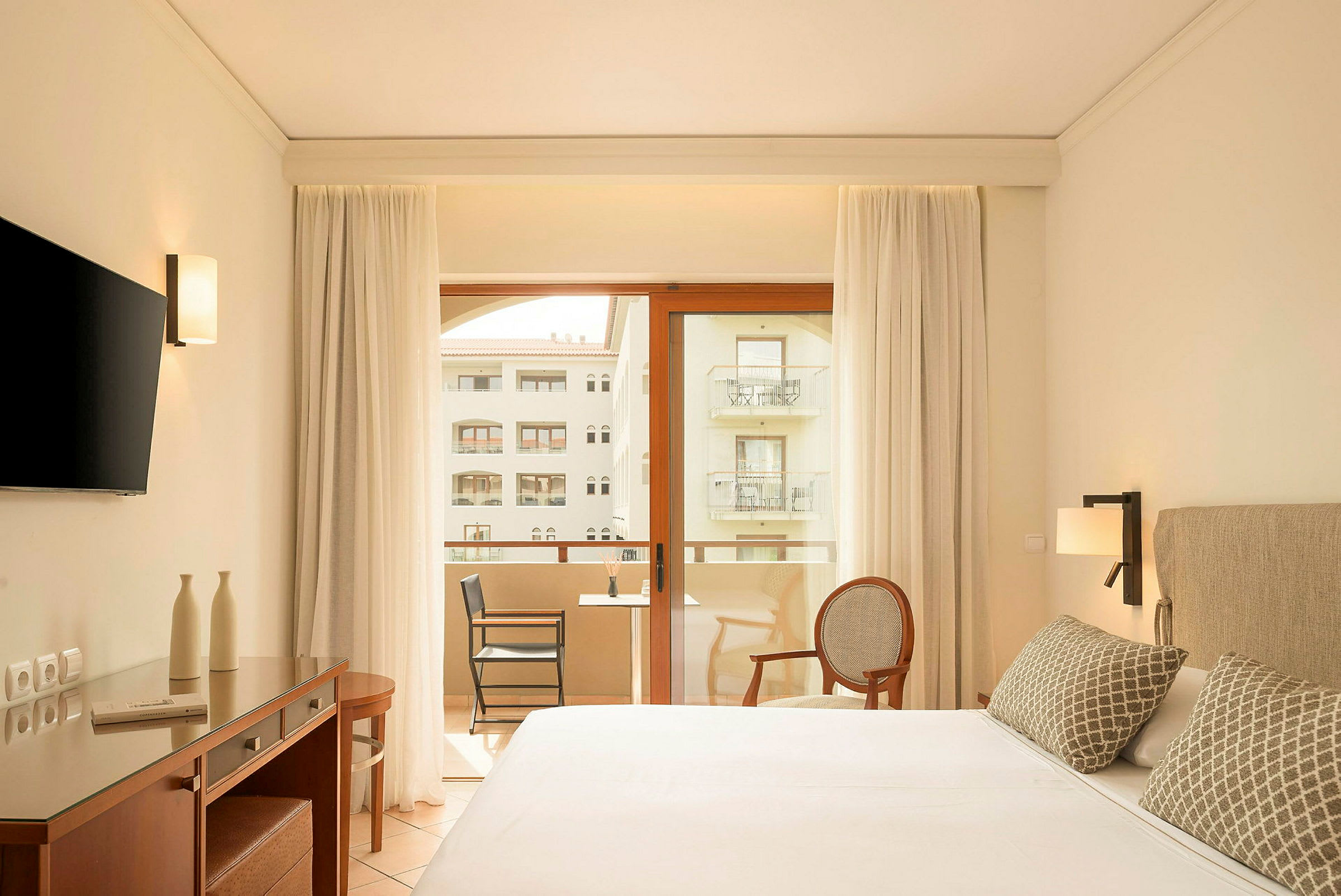 Moderne hotellrom med dobbeltseng, skrivebord, TV og balkong med utsikt. (AI-generert tekst)