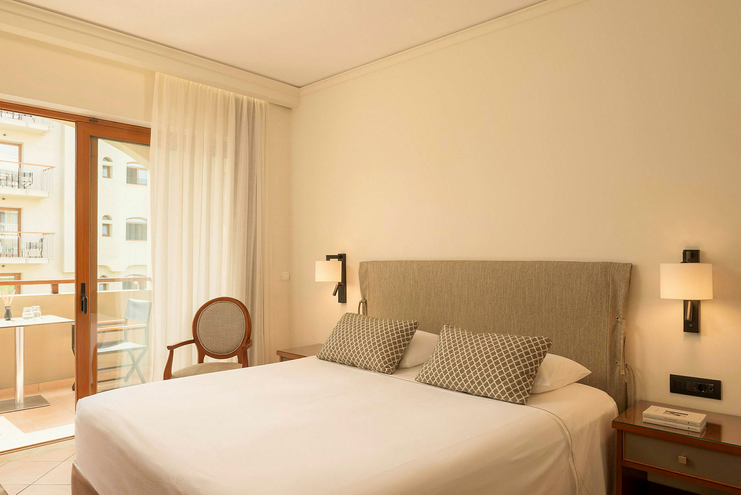 Hotellrom med en dobbeltseng, nattbord, en stol og en balkongdør med utsikt til en balkong. (AI-generert tekst)