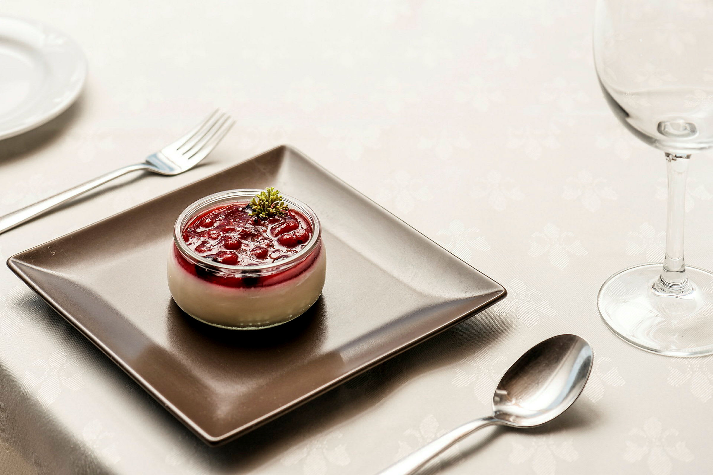 Dessert i glass med røde bær og krem, servert på svart tallerken. (AI-generert tekst)