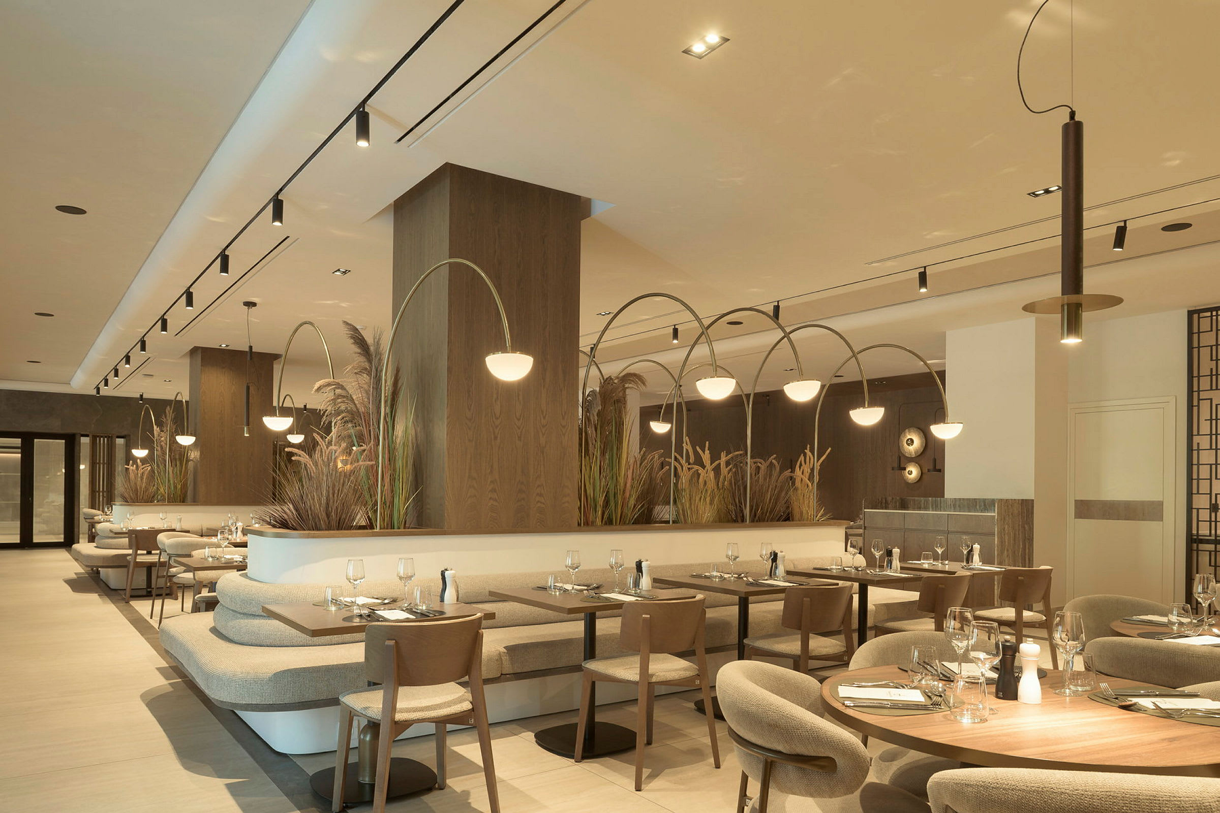Interiør av en moderne restaurant med flere bord og stoler, lys belysning og dekorative planter. (AI-generert tekst)