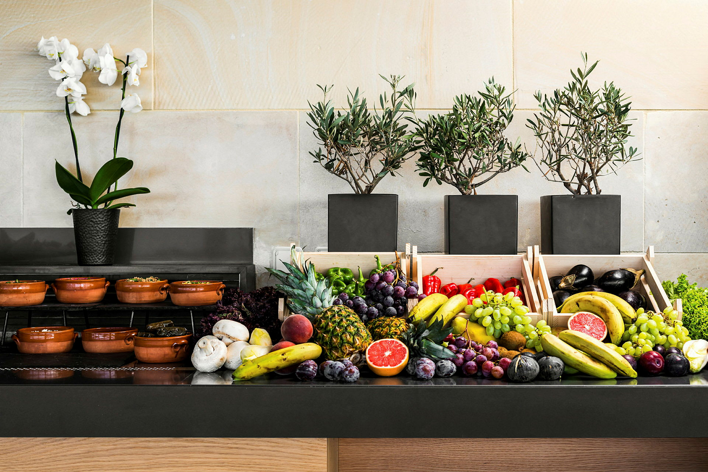 Buffetbord med frisk frukt og grønnsaker, samt olivtrær og en orkidé. (AI-generert tekst)