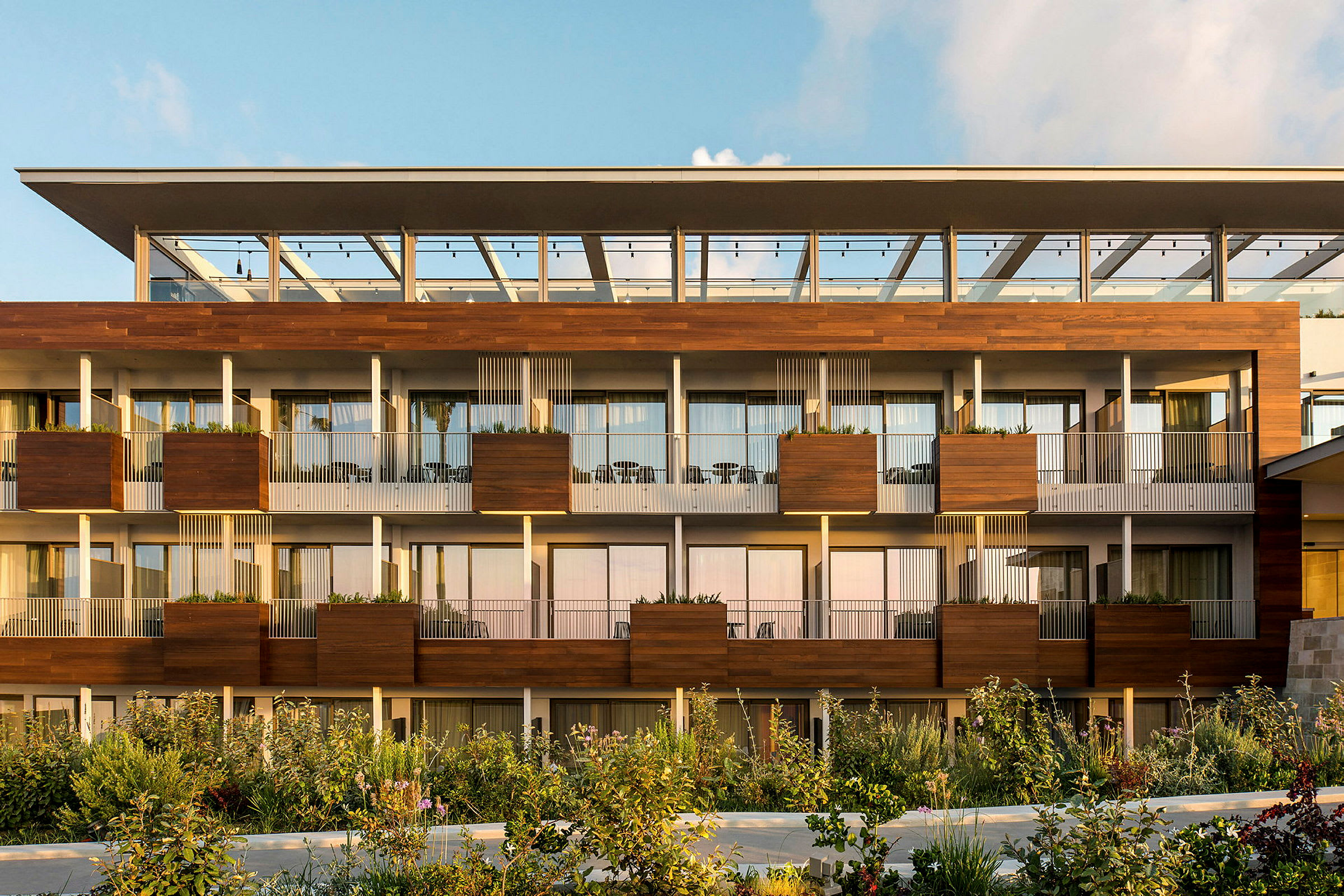 Den moderne fasaden til et hotell med balkonger og grøntareal foran. (AI-generert tekst)