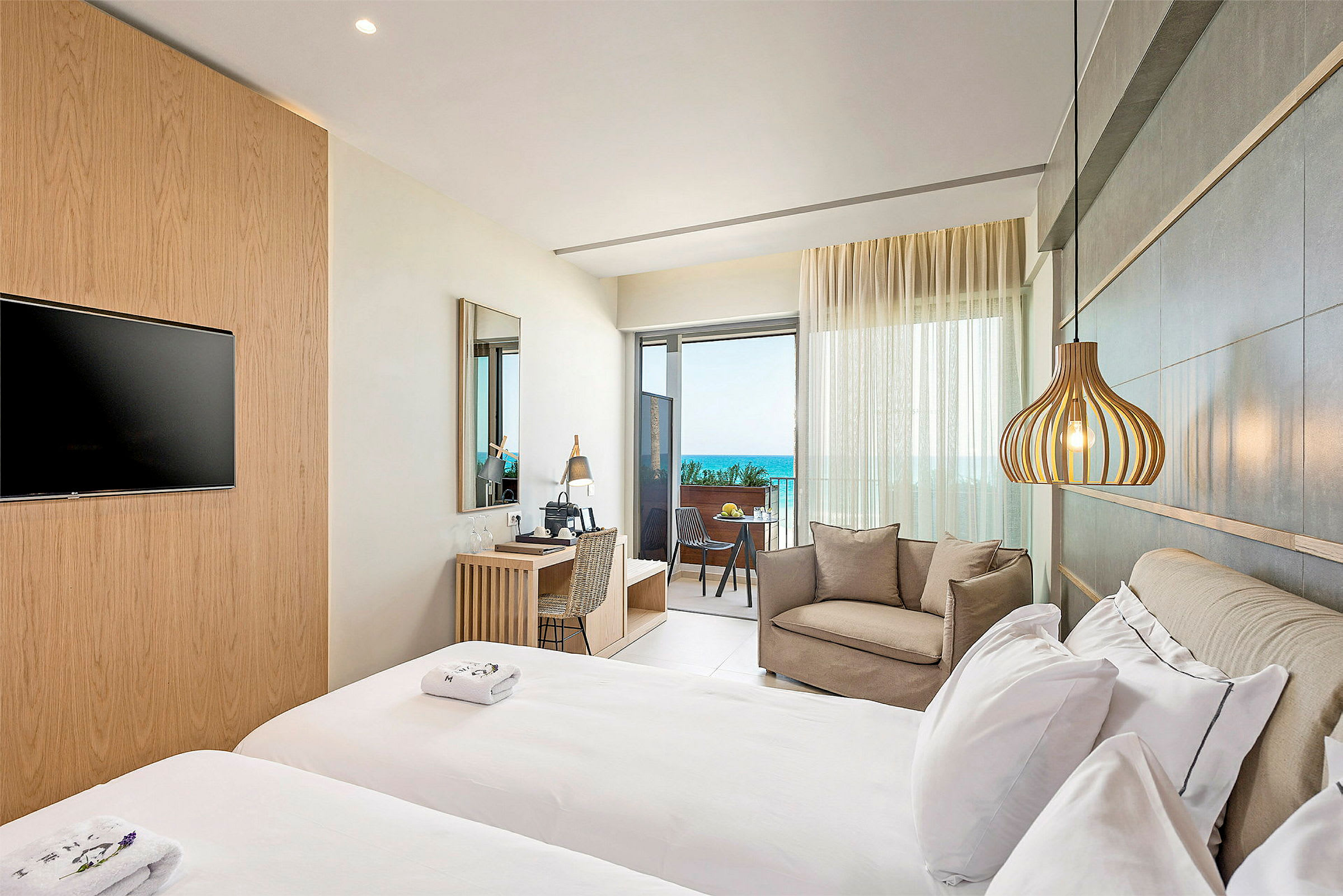 Moderne hotellrom med dobbeltseng, sittegruppe og balkong med havutsikt. (AI-generert tekst)