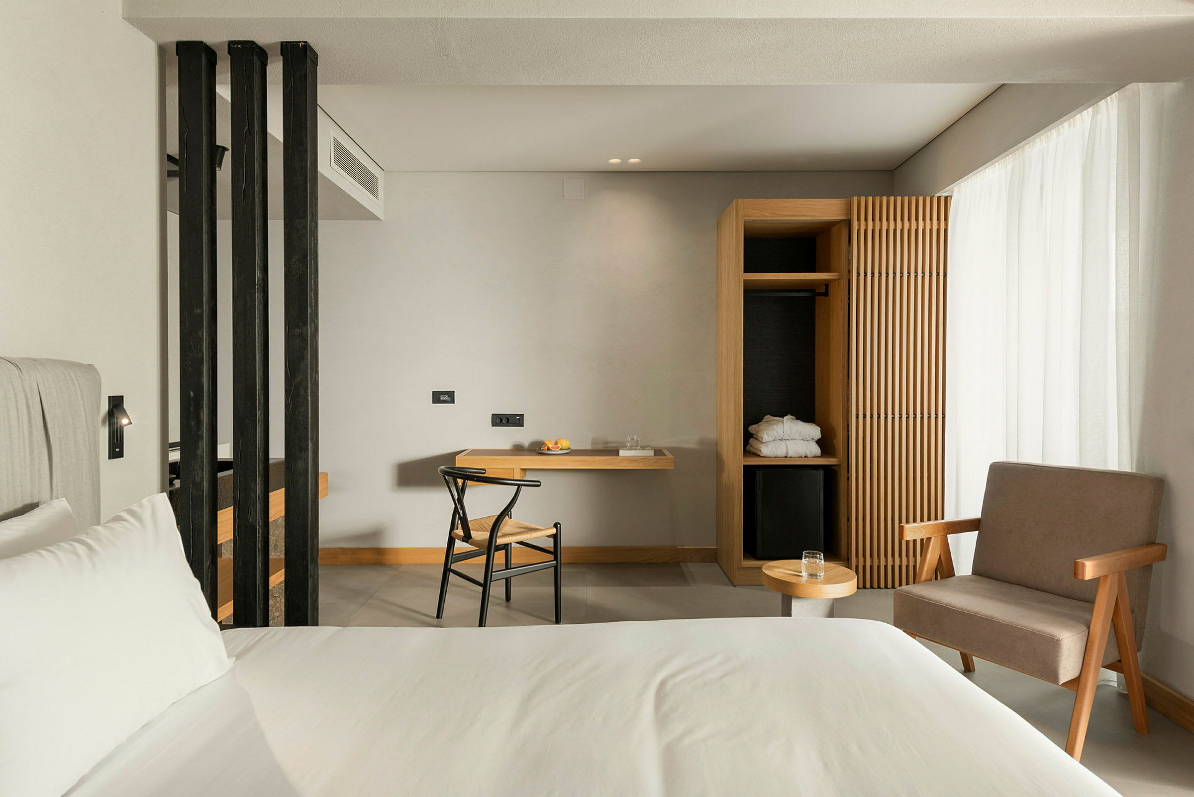 Et moderne hotellrom med en seng, en arbeidsplass med stol, og et åpent garderobeskap. (AI-generert tekst)