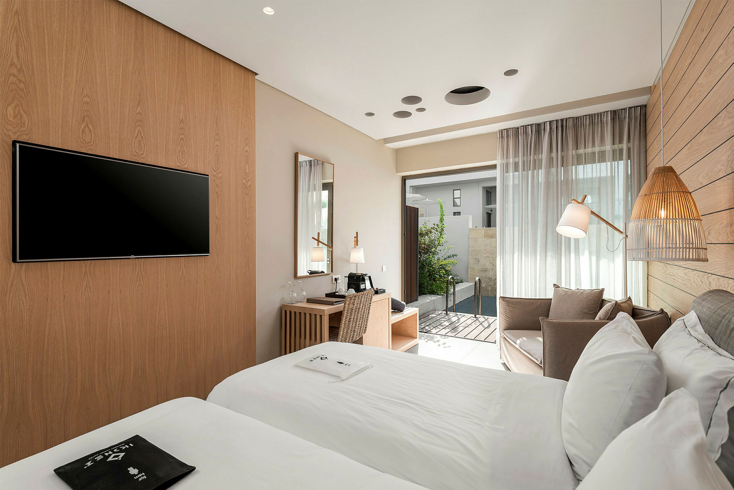 Hotellrom med to senger, skrivebord og sittegruppe. Dør som leder ut til liten basseng. (AI-generert tekst)