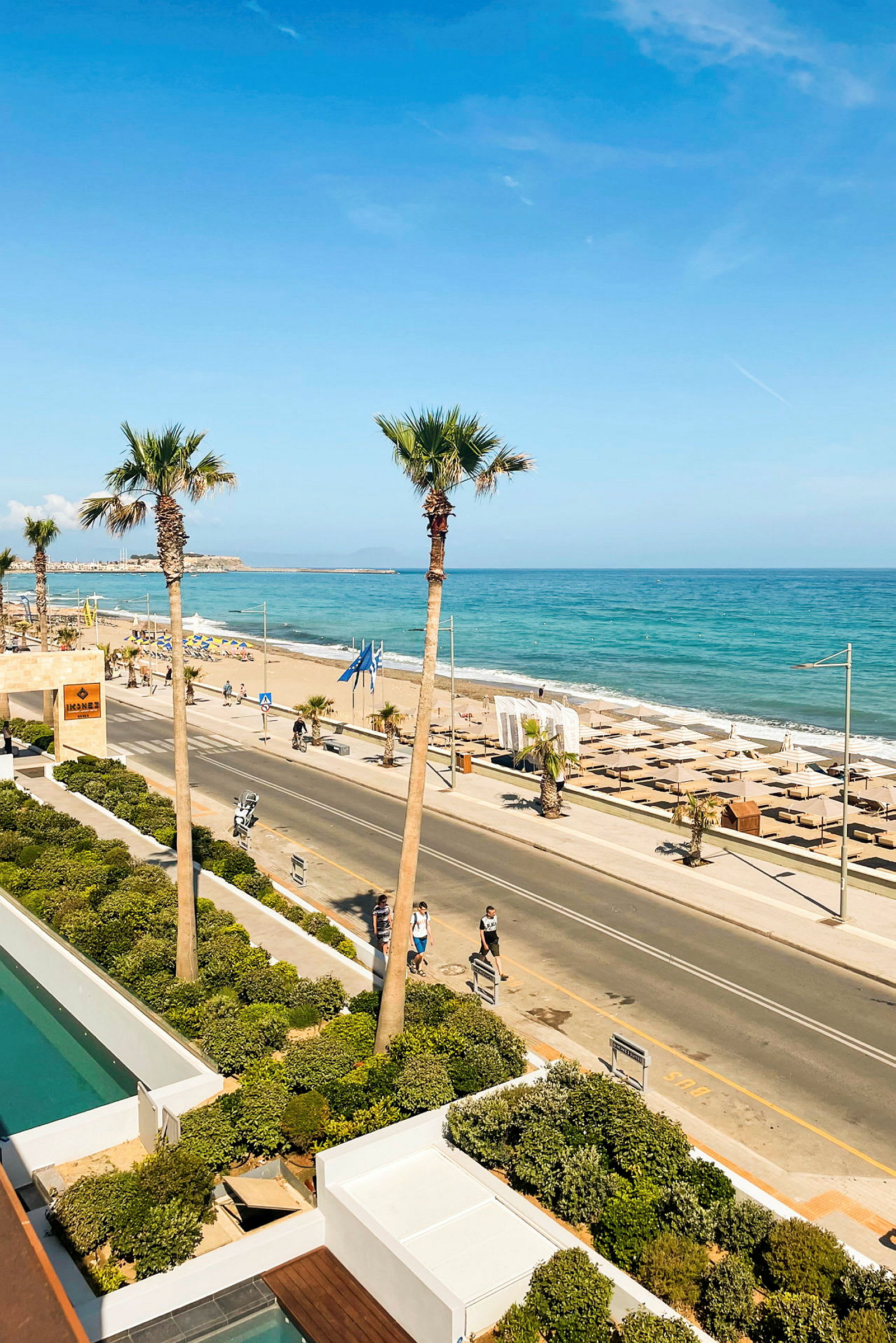 Utsikt over en strandpromenade med palmer, en vei og stranden ved havet. (AI-generert tekst)
