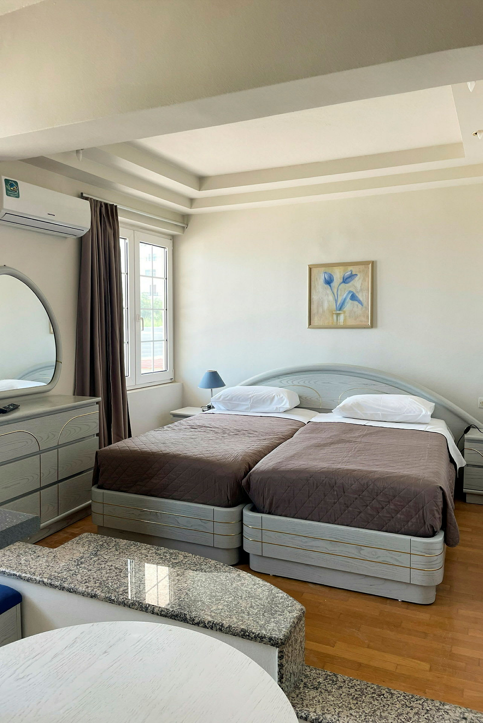 Hotellrom med to enkeltsenger, et skrivebord og et speil. (AI-generert tekst)
