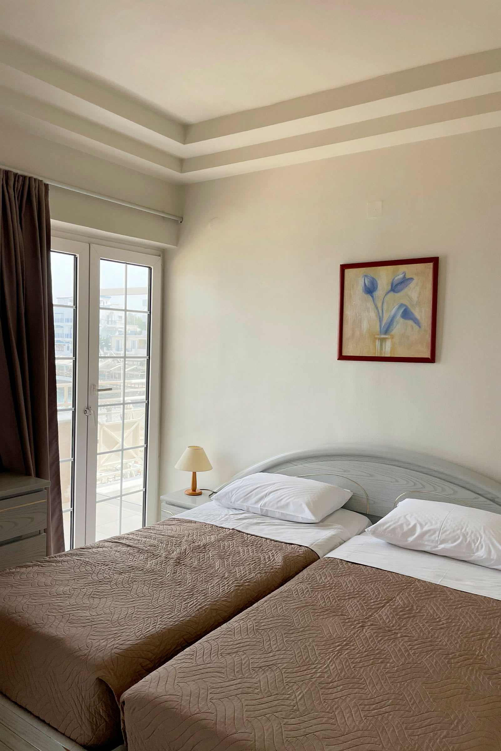 Et hotellrom med to enkeltsenger, en lampe og en glassdør. (AI-generert tekst)