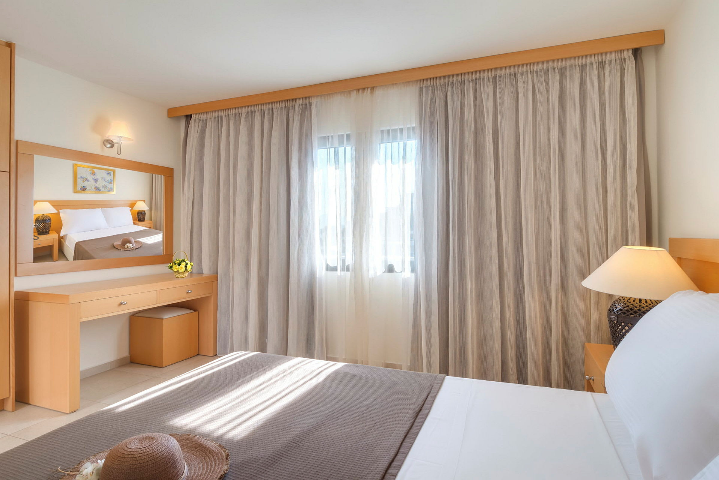 Et hotellrom med en seng, et speil og gardiner over et vindu. (AI-generert tekst)