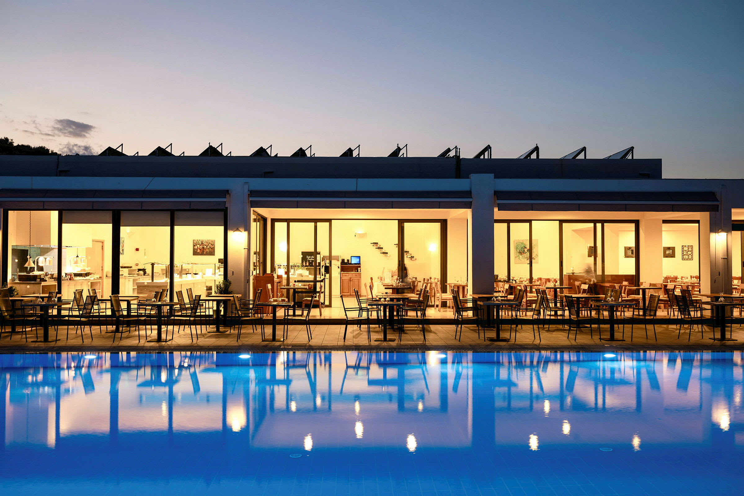 Hotellrestaurant med uteservering om kvelden, med utsikt over et opplyst basseng. (AI-generert tekst)
