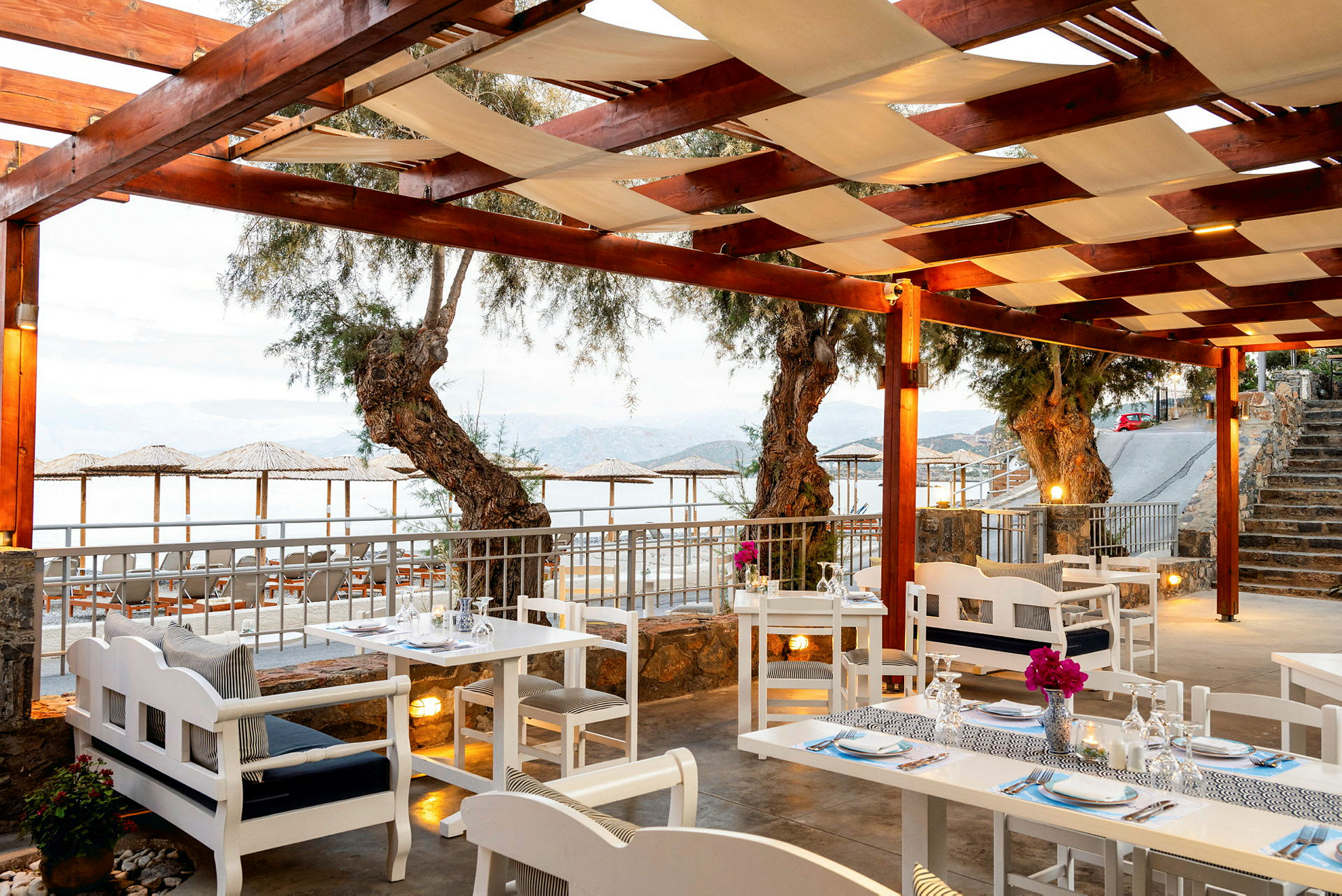 Restaurant med hvite bord og stoler under en trepergola med utsikt over havet. (AI-generert tekst)
