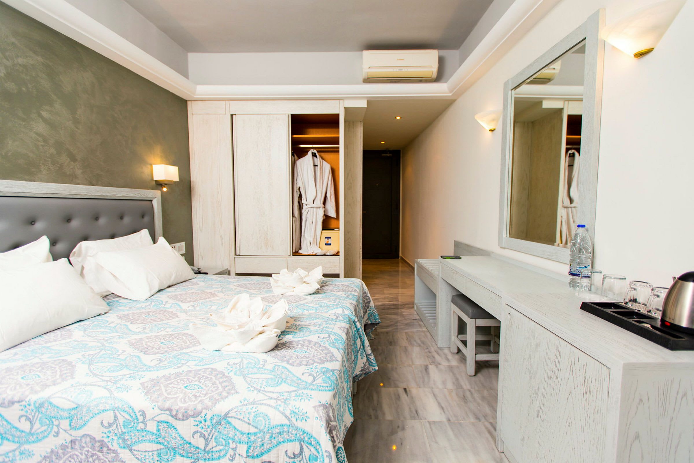 Hotellrom med dobbeltseng, et speil over en skrivebord og en åpen garderobe med badekåper. (AI-generert tekst)