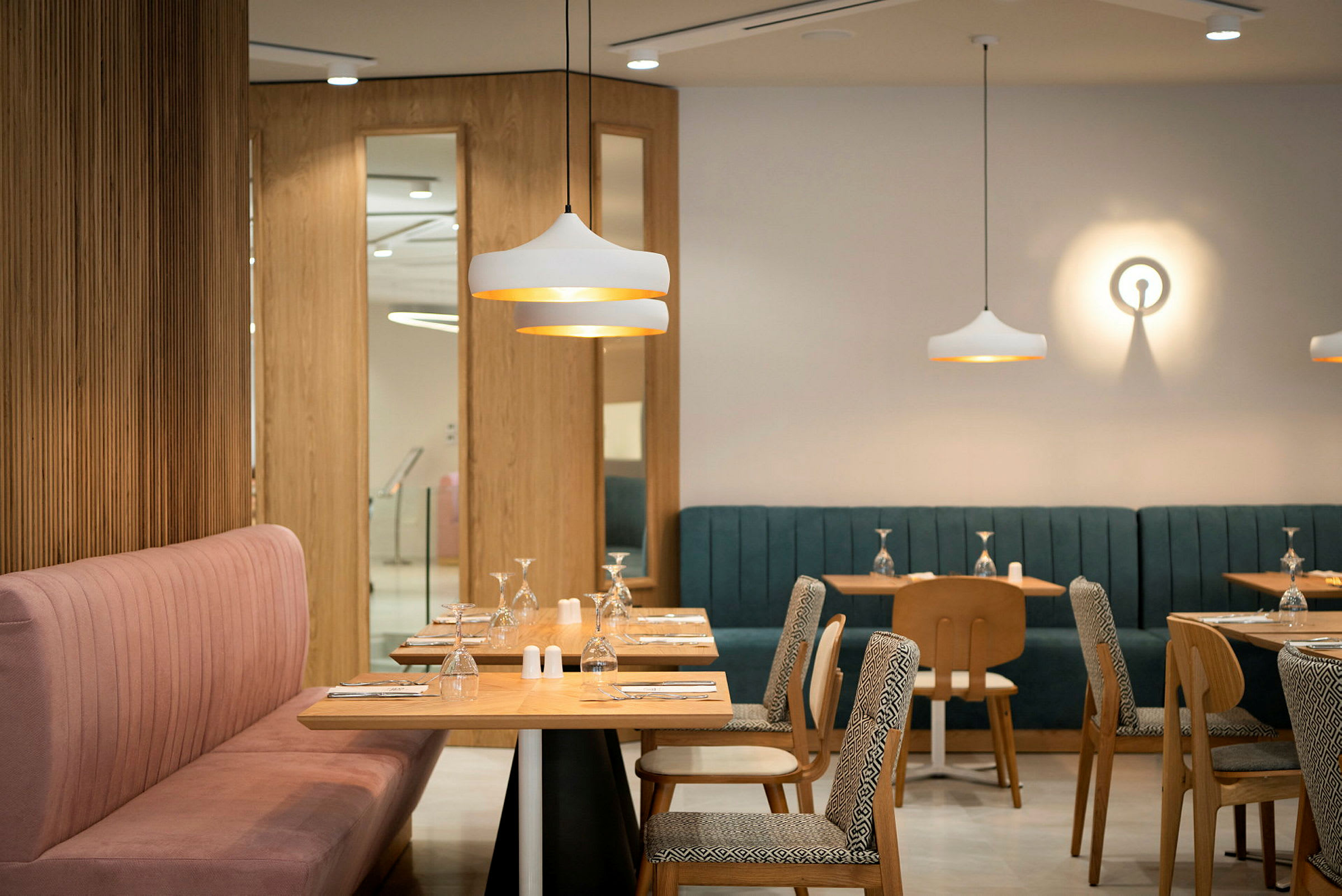 En moderne restaurant med bord og stoler i tre, fargerike polstrede sofaer og dekorative lysarmaturer. (AI-generert tekst)
