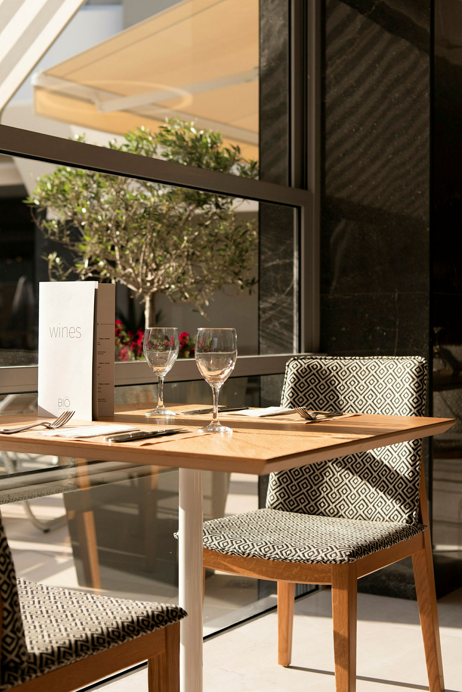 Et dekket bord med to glass og en meny ved vinduet. (AI-generert tekst)