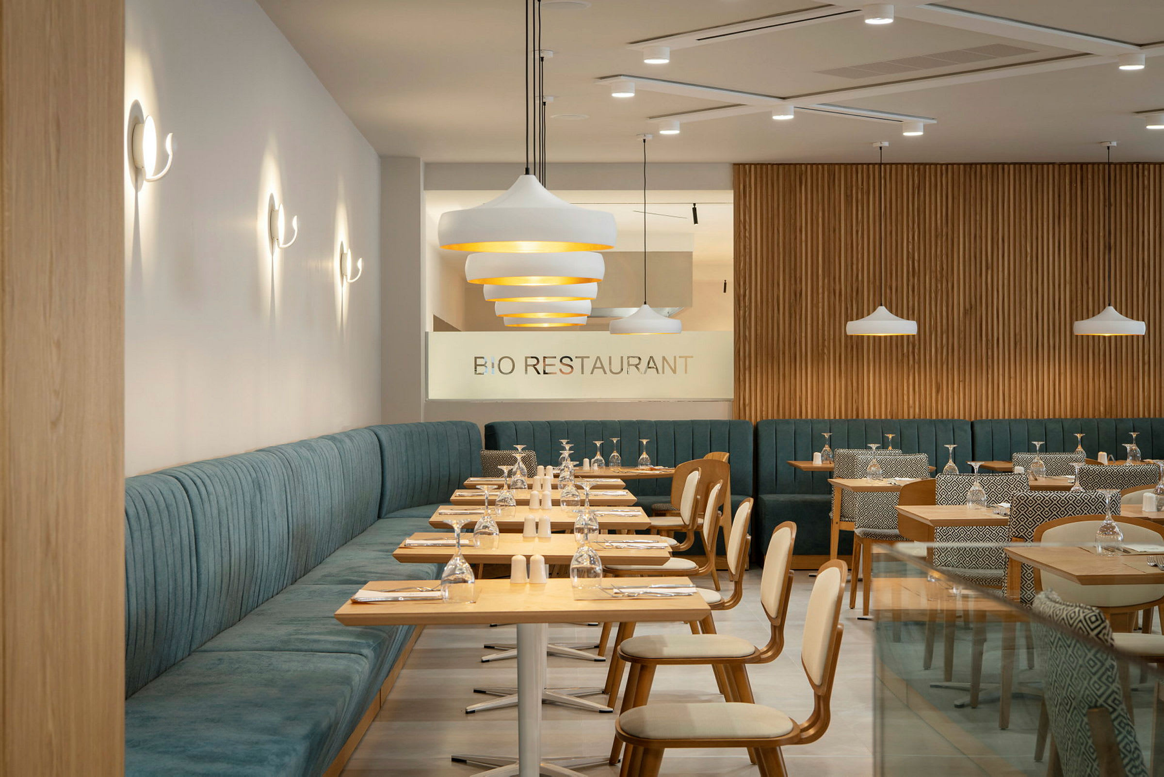 Moderne restaurant med trebord og polstrede sitteplasser. Glass og tallerkener er arrangert på bordene. (AI-generert tekst)