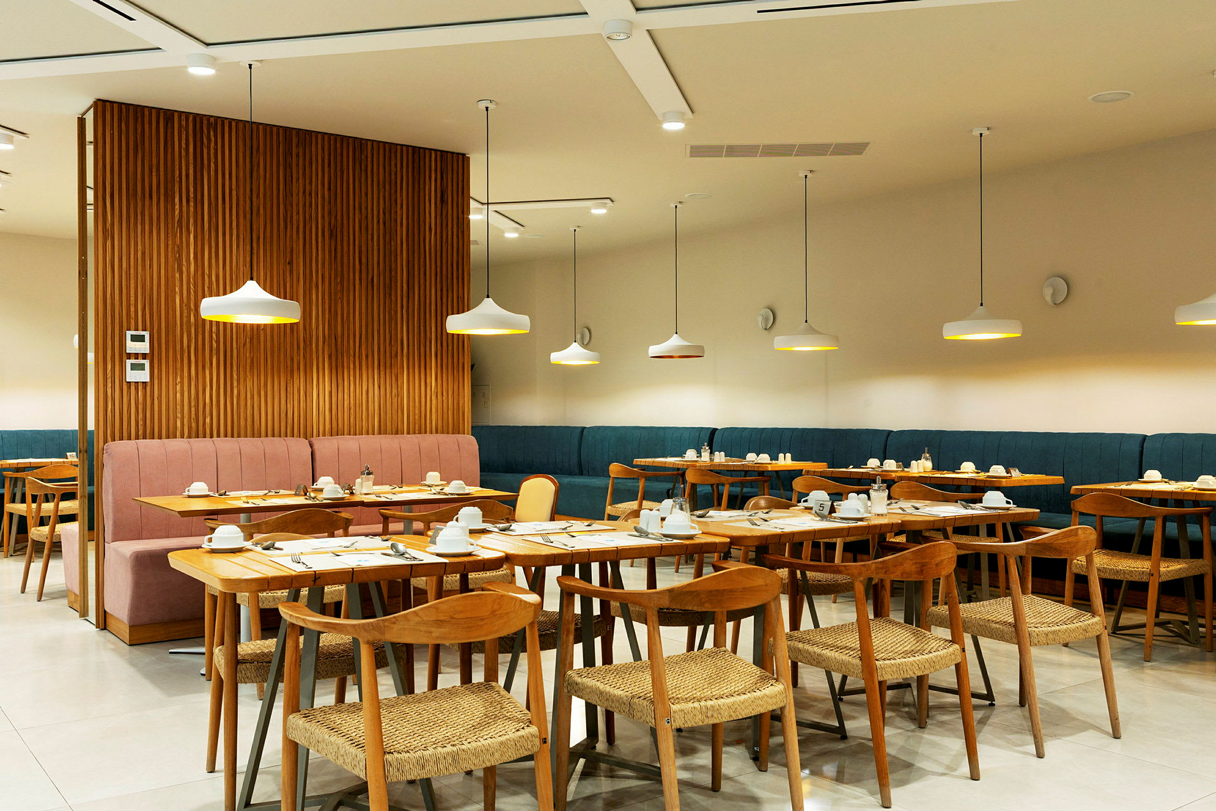 En moderne innendørsrestaurant med bord og stoler laget av tre, samt stilfullt plasserte taklamper. (AI-generert tekst)