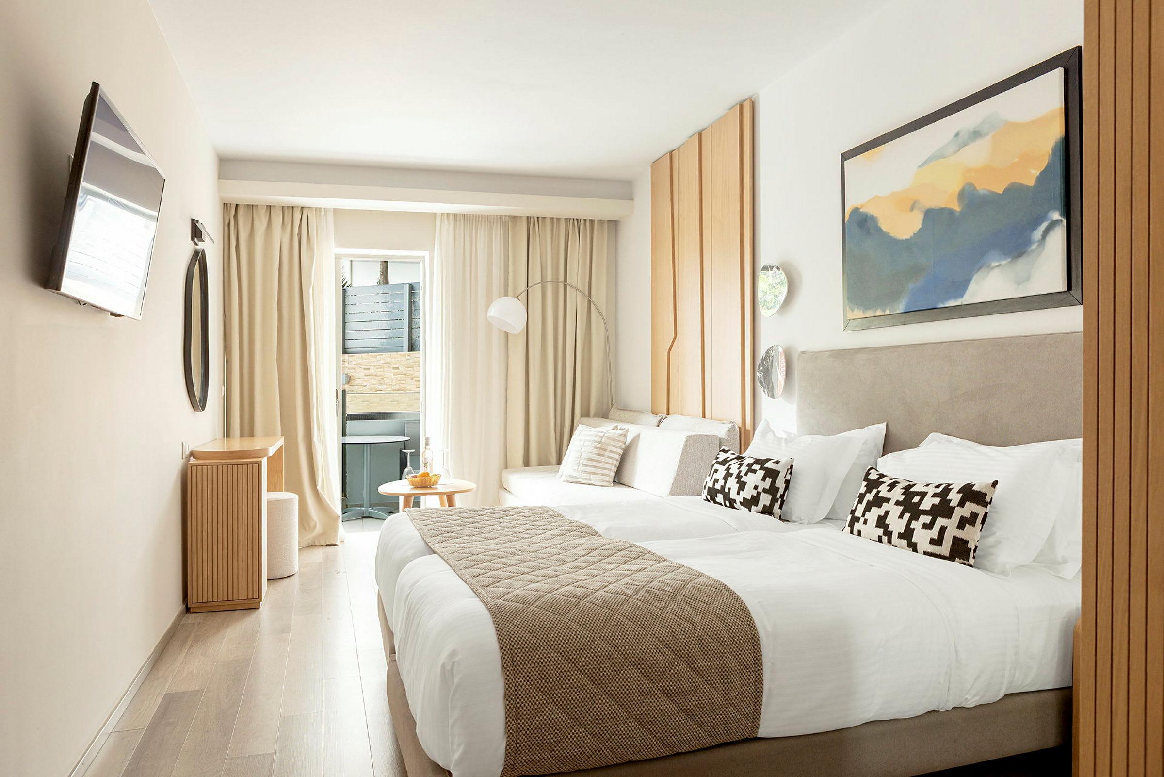 Et moderne hotellrom med en dobbeltseng, lyse møbler og dekorasjoner samt en liten sittegruppe nær et vindu. (AI-generert tekst)