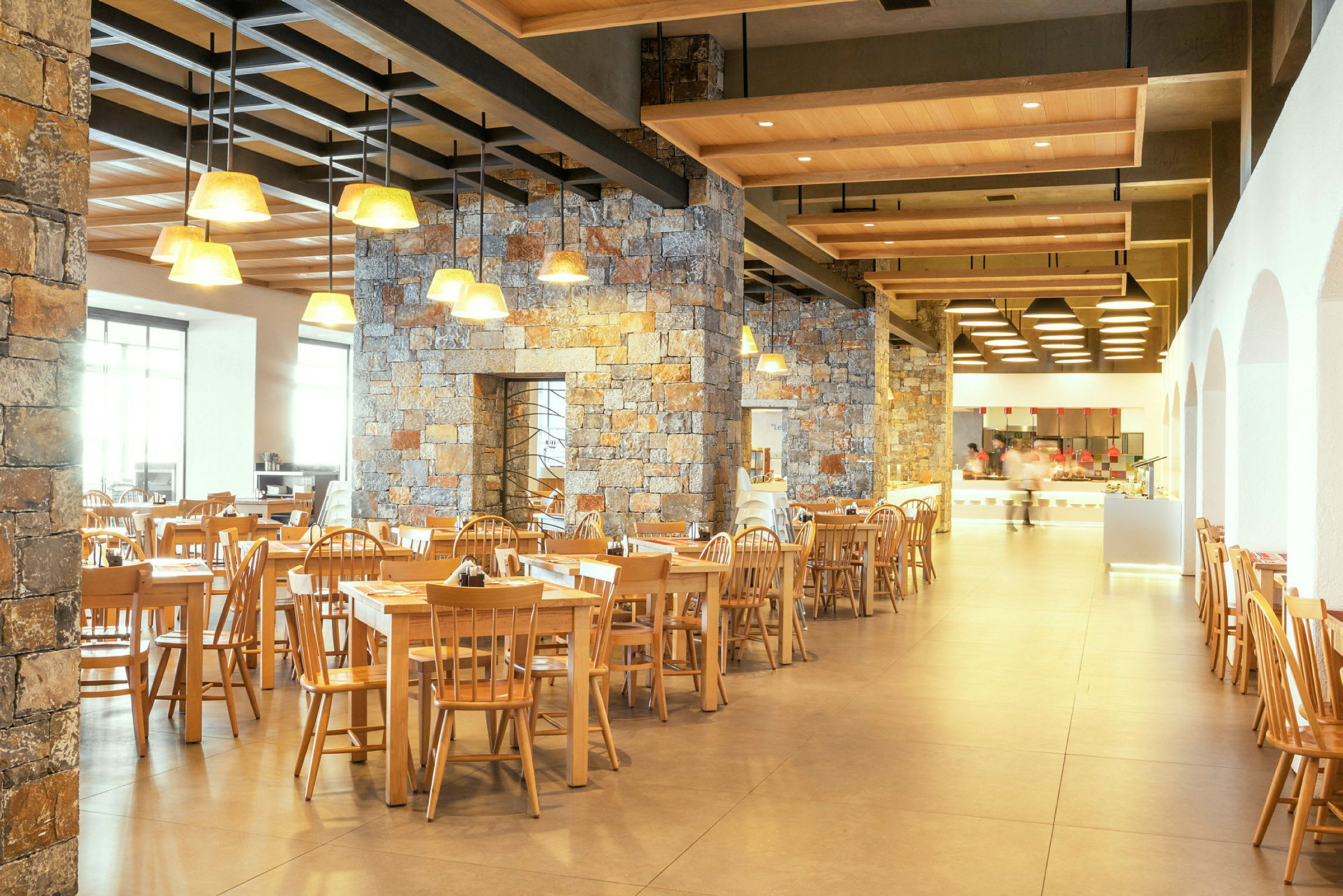 Restaurant med tredestoler og bord samt steinvegger og taklamper. (AI-generert tekst)